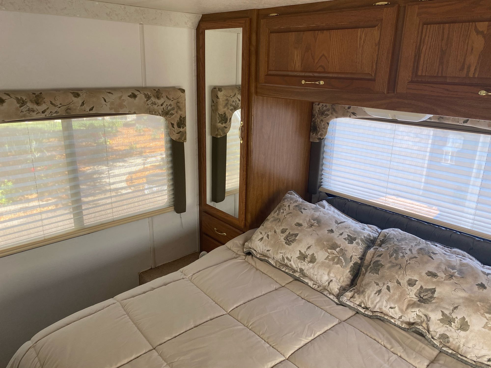 RV rental bedroom interior: comfy bed, patterned pillows, windows with blinds, wood cabinets, and a full-length mirror.. Dutchmen Four Winds 2003