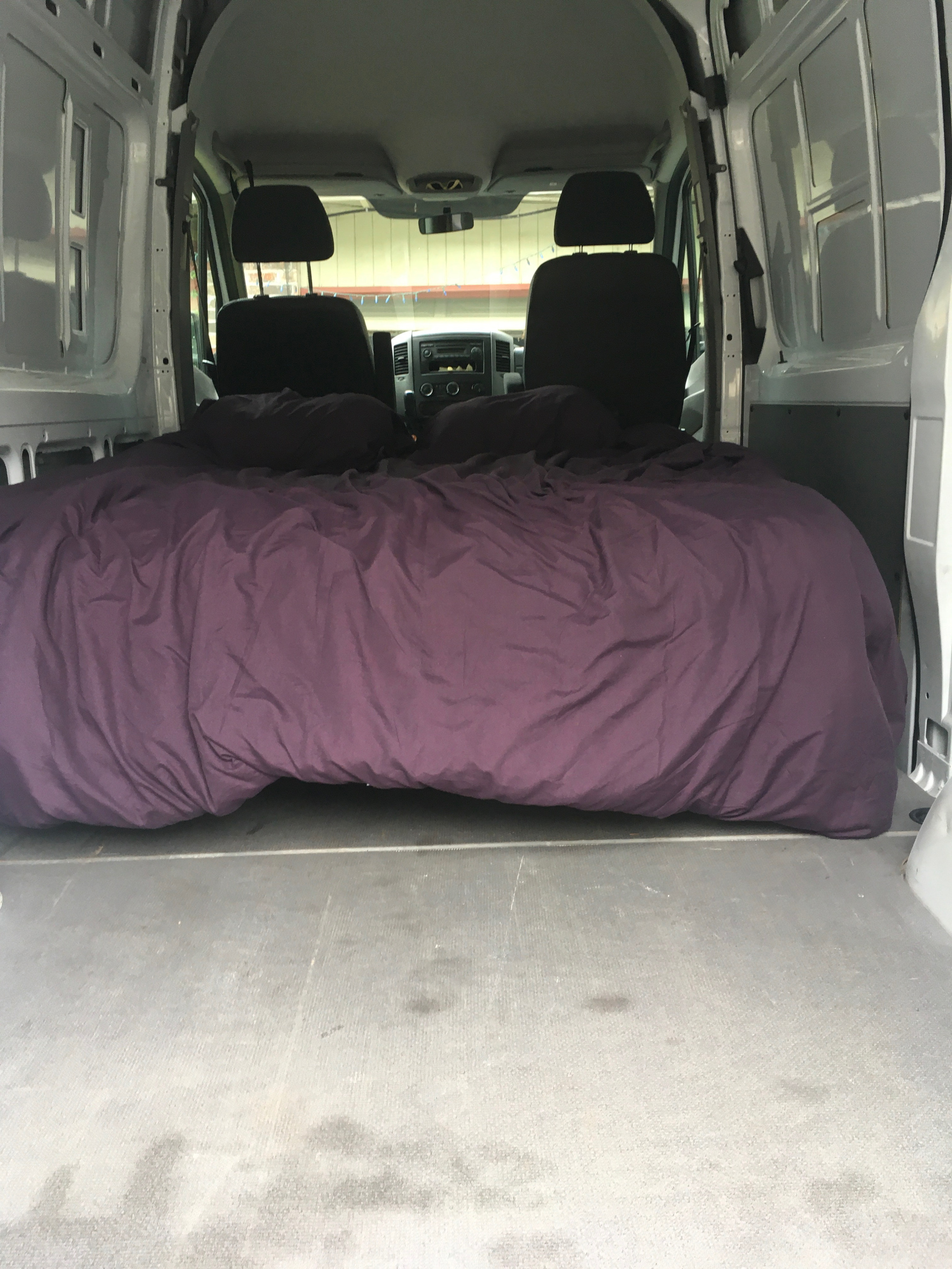Cozy rv rental van interior featuring a large purple bed, ready for your next adventure. Driver's cabin visible.. Mercedes-Benz Sprinter 2013