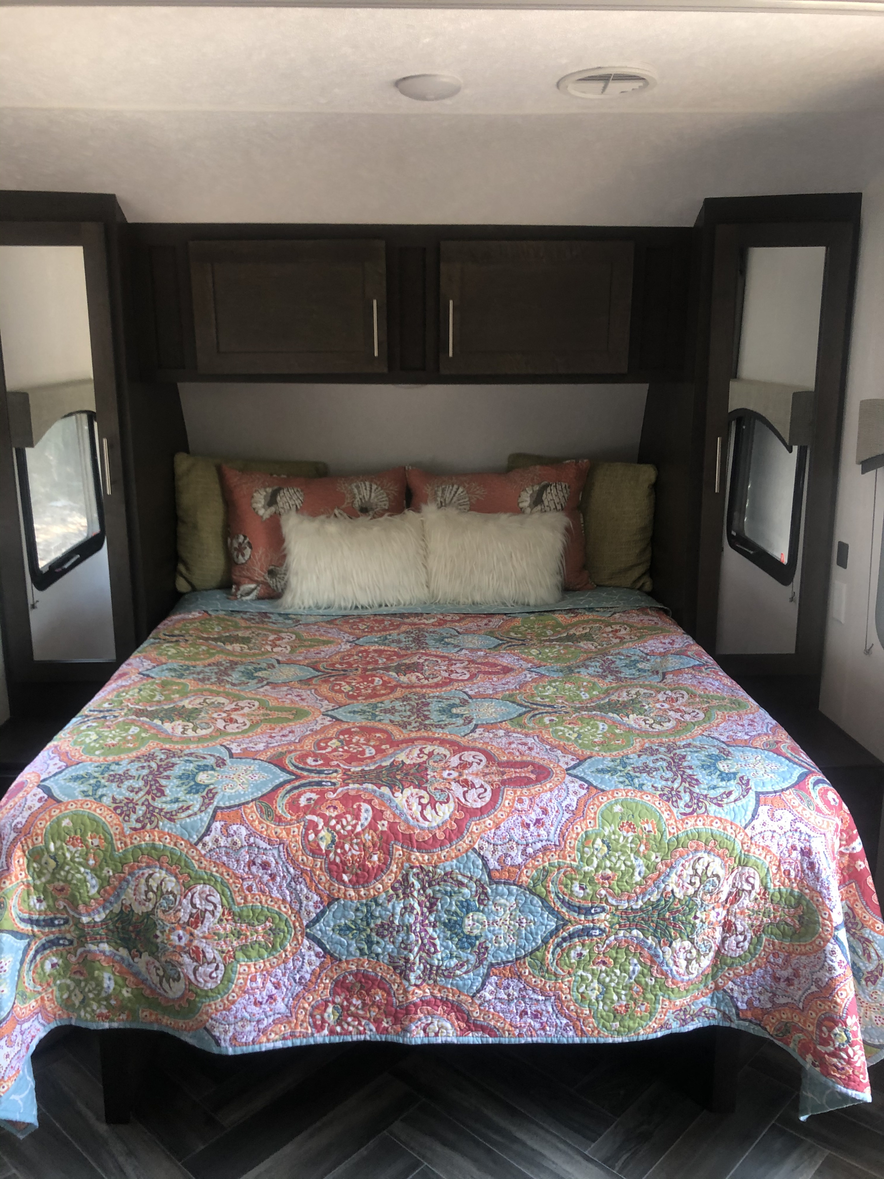 Cozy RV rental bedroom featuring a queen bed, colorful quilt, pillows, built-in cabinets, and side windows.. Forest River Evo 2019