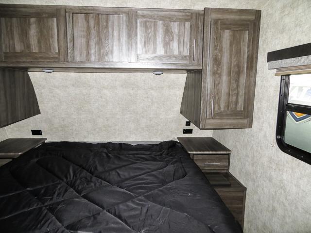 RV rental bedroom with a bed featuring a black comforter, overhead wood cabinets, side storage, and a window.. Open Range Open Range 2018