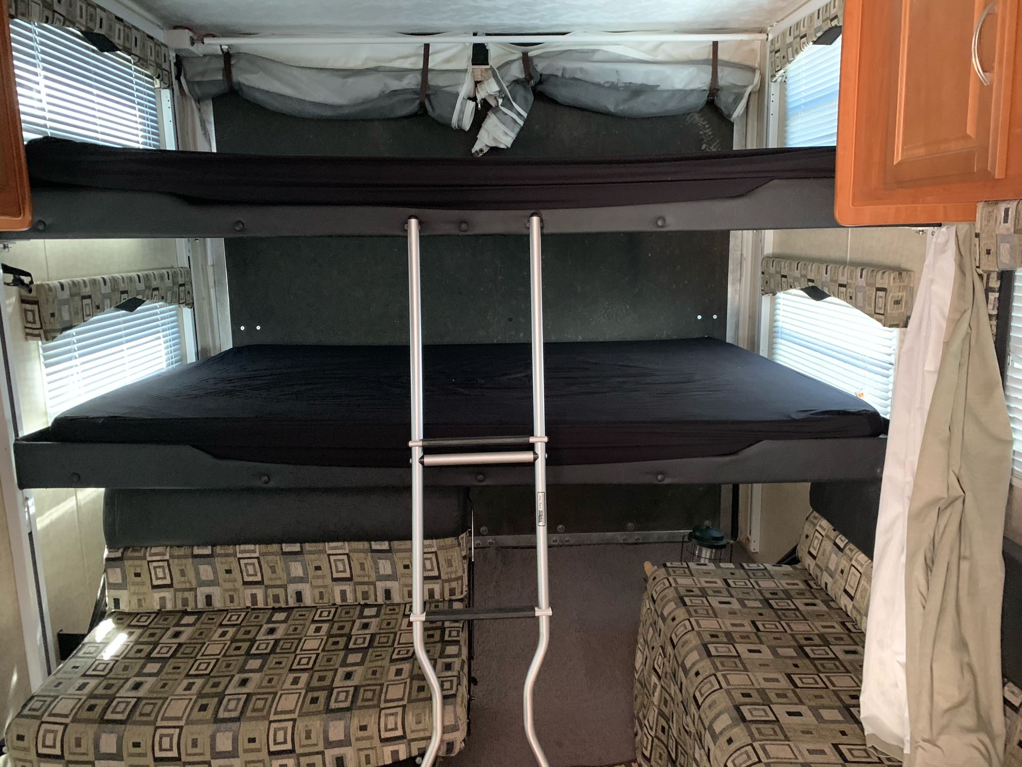 Inside an RV rental, showing the sleeping area with two bunk beds and a ladder. Comfortable seating below windows.. ForestRiver Sandstorm 2008