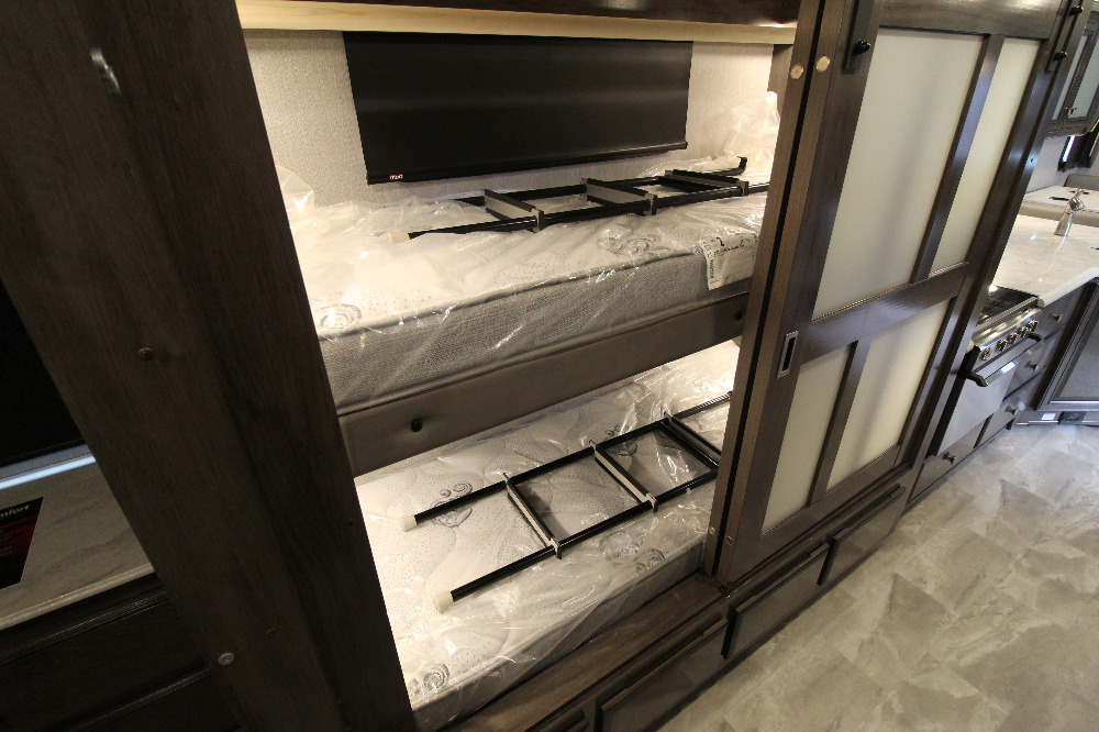 Modern RV rental interior showcasing bunk beds with plastic-covered mattresses and an adjacent kitchen area, ready for travel.. Dynamax Corp Dx3 2020