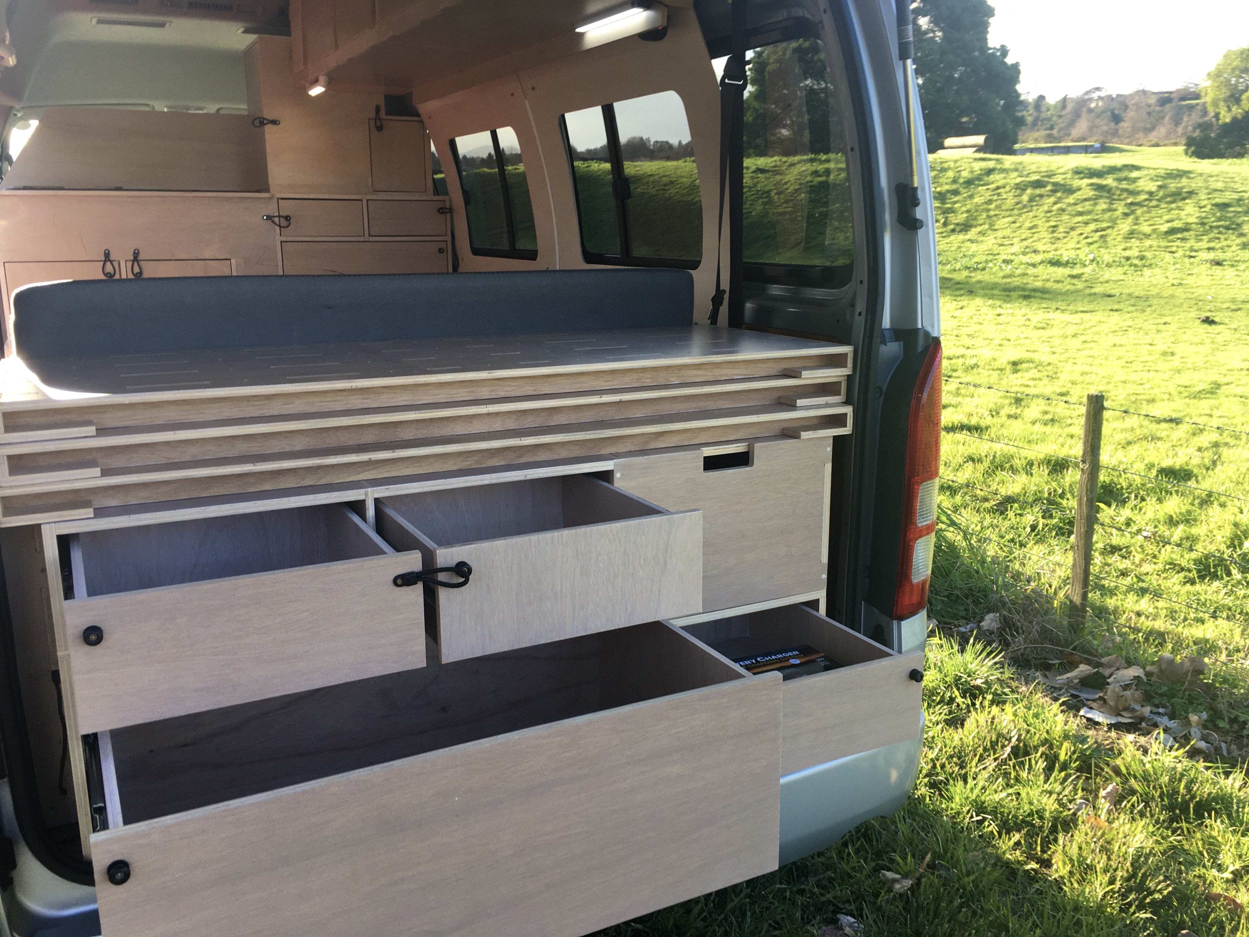 Custom-built wood interior of an RV rental, showcasing clever storage drawers & pull-out bed system.. Toyota Hiace 2006
