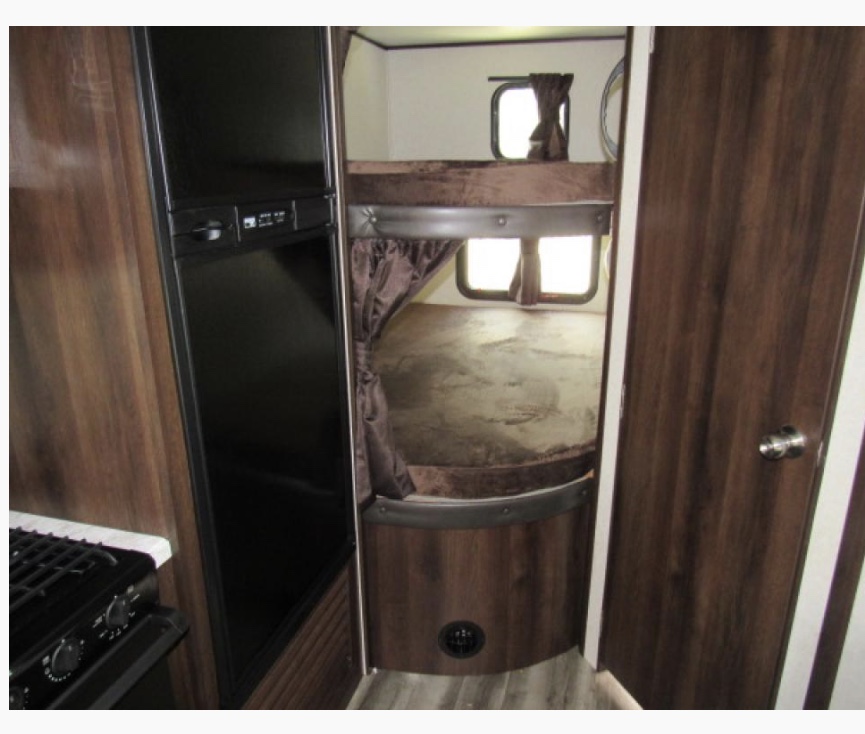 Interior view of an RV rental: includes bunk beds with curtains, a refrigerator, and stove. Ideal for family trips.. Jayco Jay Flight 2021