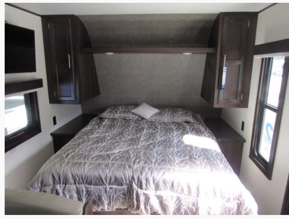 RV rental bedroom with a comfortable bed, dark wood cabinets, and ample natural light from windows.. Jayco Jay Flight 2021
