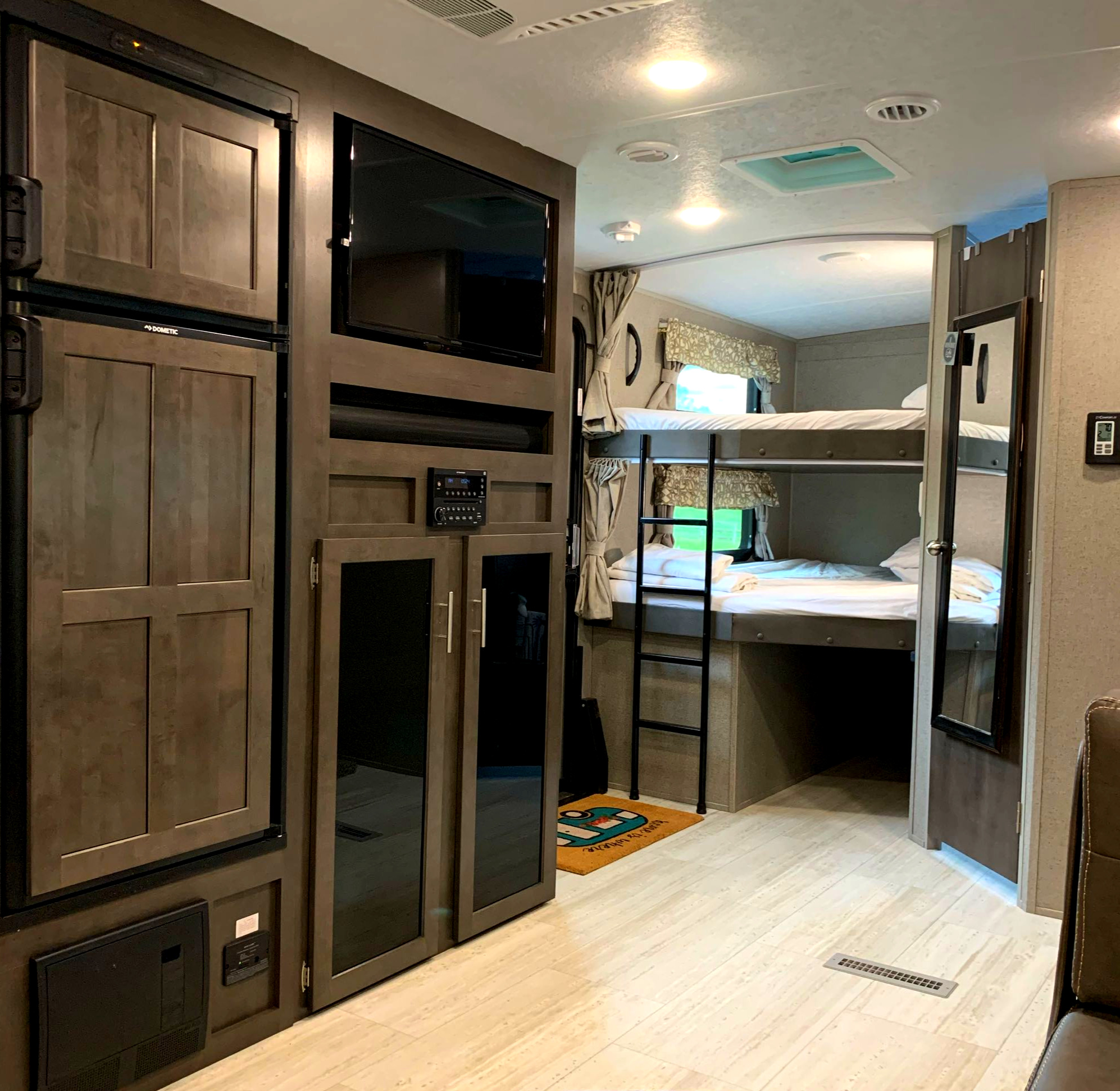 Bright RV rental interior with a Dometic fridge, entertainment center (TV, stereo), and comfortable bunk beds with a ladder.. Forest River Rockwood Ultra Lite 2020