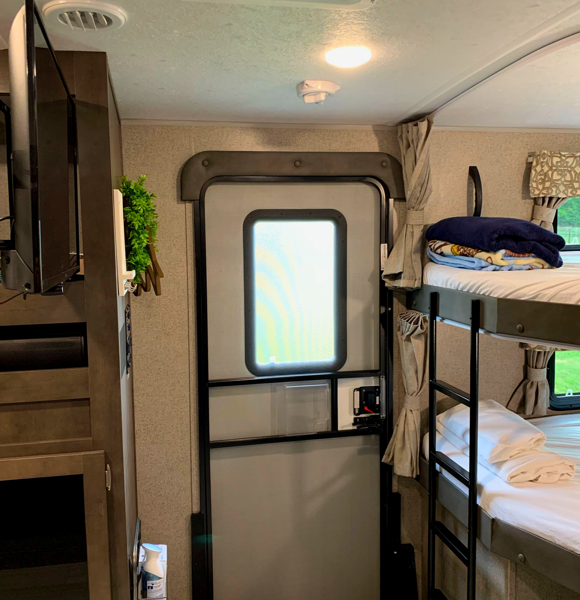 Inside an RV rental, featuring bunk beds, an interior door, a mounted TV, and ceiling details like an AC vent and smoke detector.. Forest River Rockwood Ultra Lite 2020