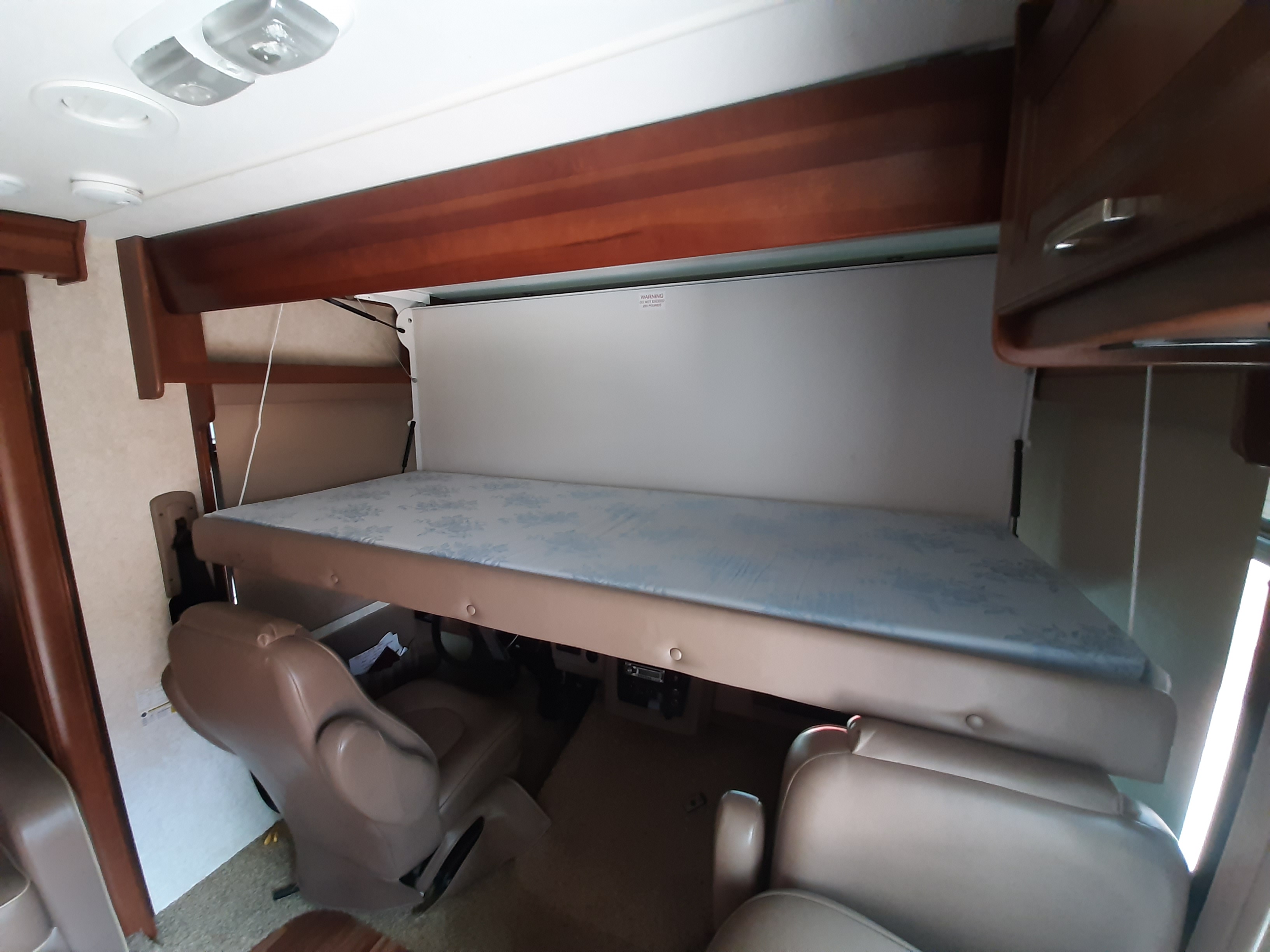 RV rental motorhome interior showing a lowered bunk bed above two tan captain's chairs, maximizing sleeping space.. Forest River Georgetown 2014