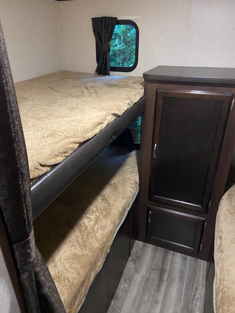 RV rental interior featuring stacked bunk beds with tan bedding, a window with curtains, and a dark wood storage cabinet.. Jayco Other 2018
