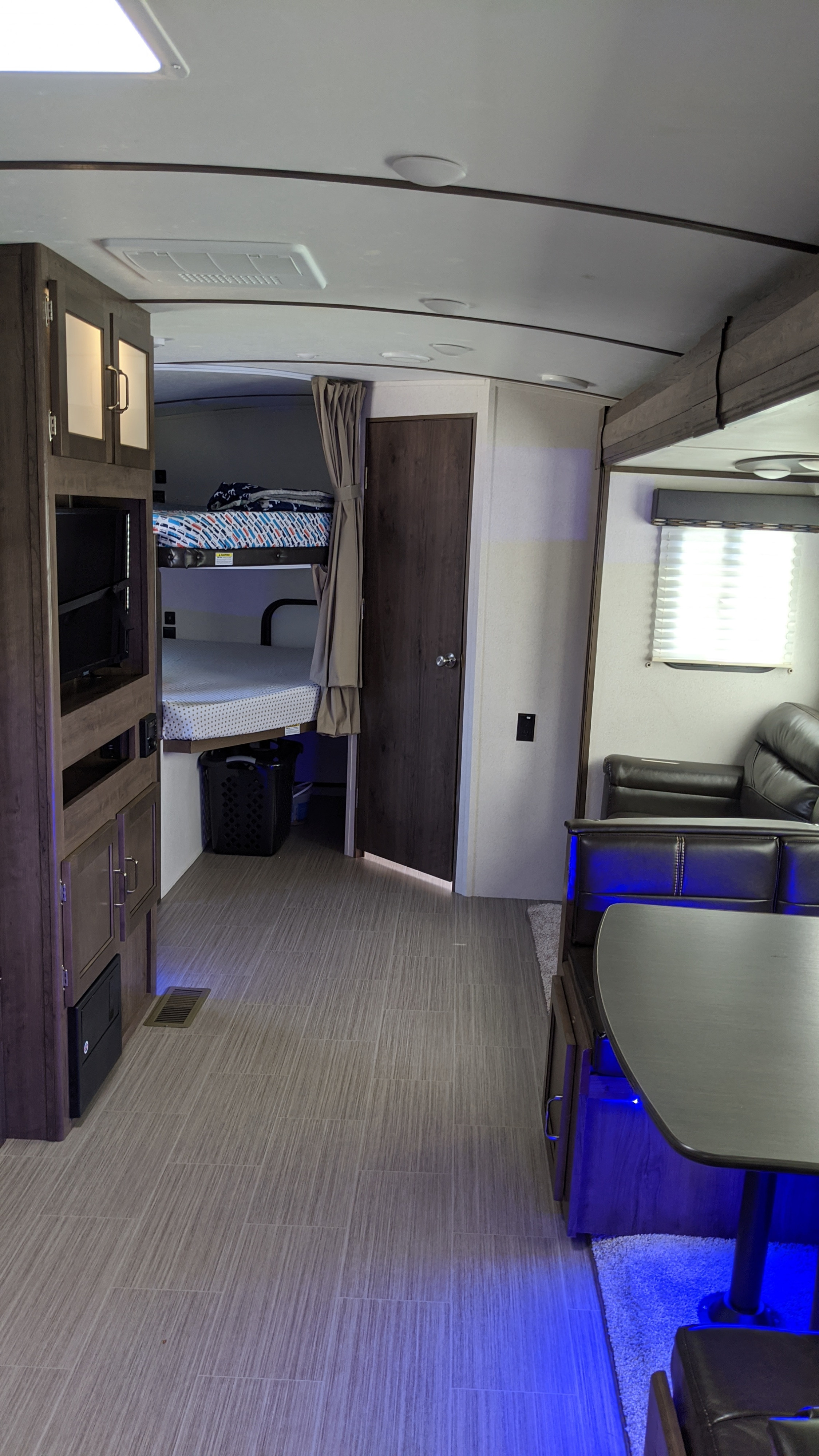 Inside an rv rental, showcasing the living space with a blue-lit dinette, bunk beds, and entertainment unit.. Keystone RV Passport Grand Touring 2020