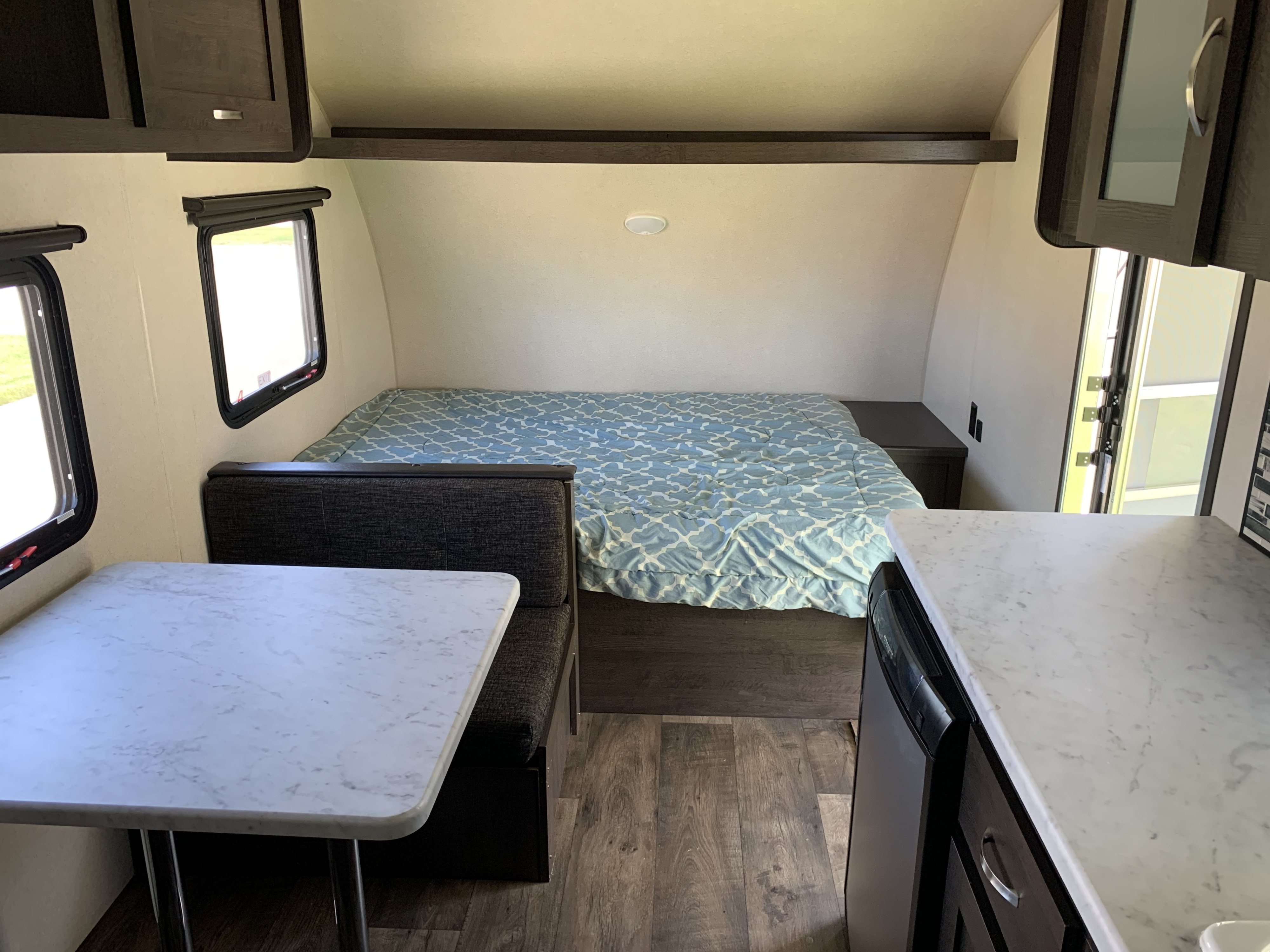 View inside an rv rental showing a bed with blue comforter, dinette, and kitchen counter.. Forest River Wildwood 2019