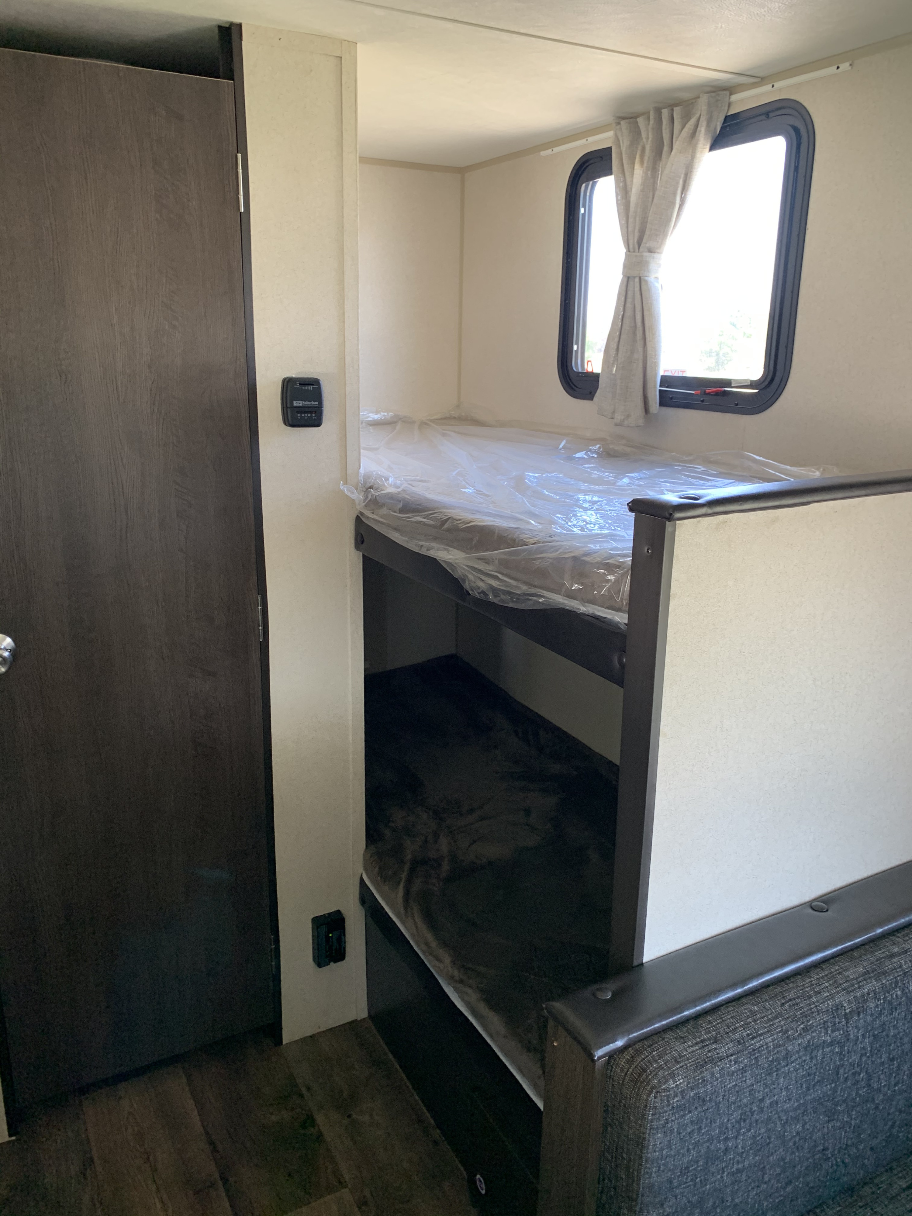 Interior of an RV rental showing cozy bunk beds, a window with curtains, and a door, ideal for family trips.. Forest River Wildwood 2019