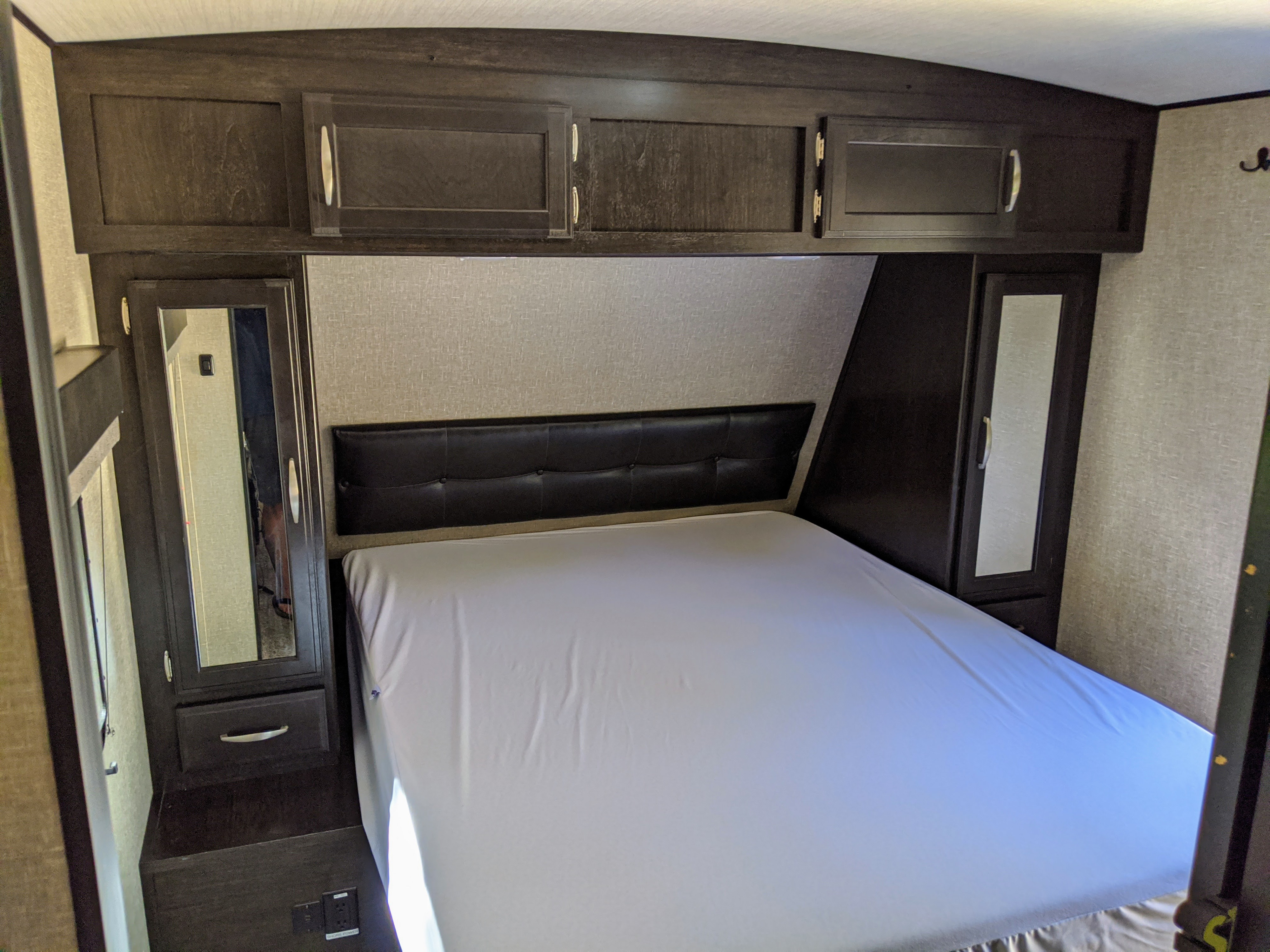 RV rental bedroom with a cozy bed, dark wood overhead cabinets, and mirrored closets, offering comfort and practical storage.. Grand Design Imagine 2019