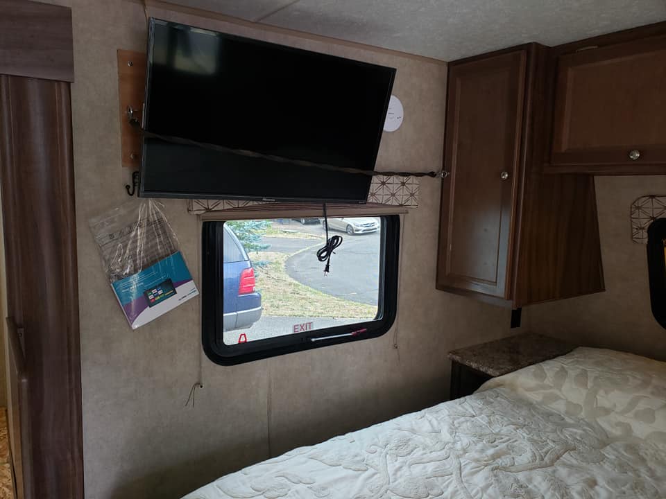 Cozy RV rental bedroom with a wall-mounted TV, comfy bed, window view, and overhead wooden cabinets.. Forest River Viking 2017