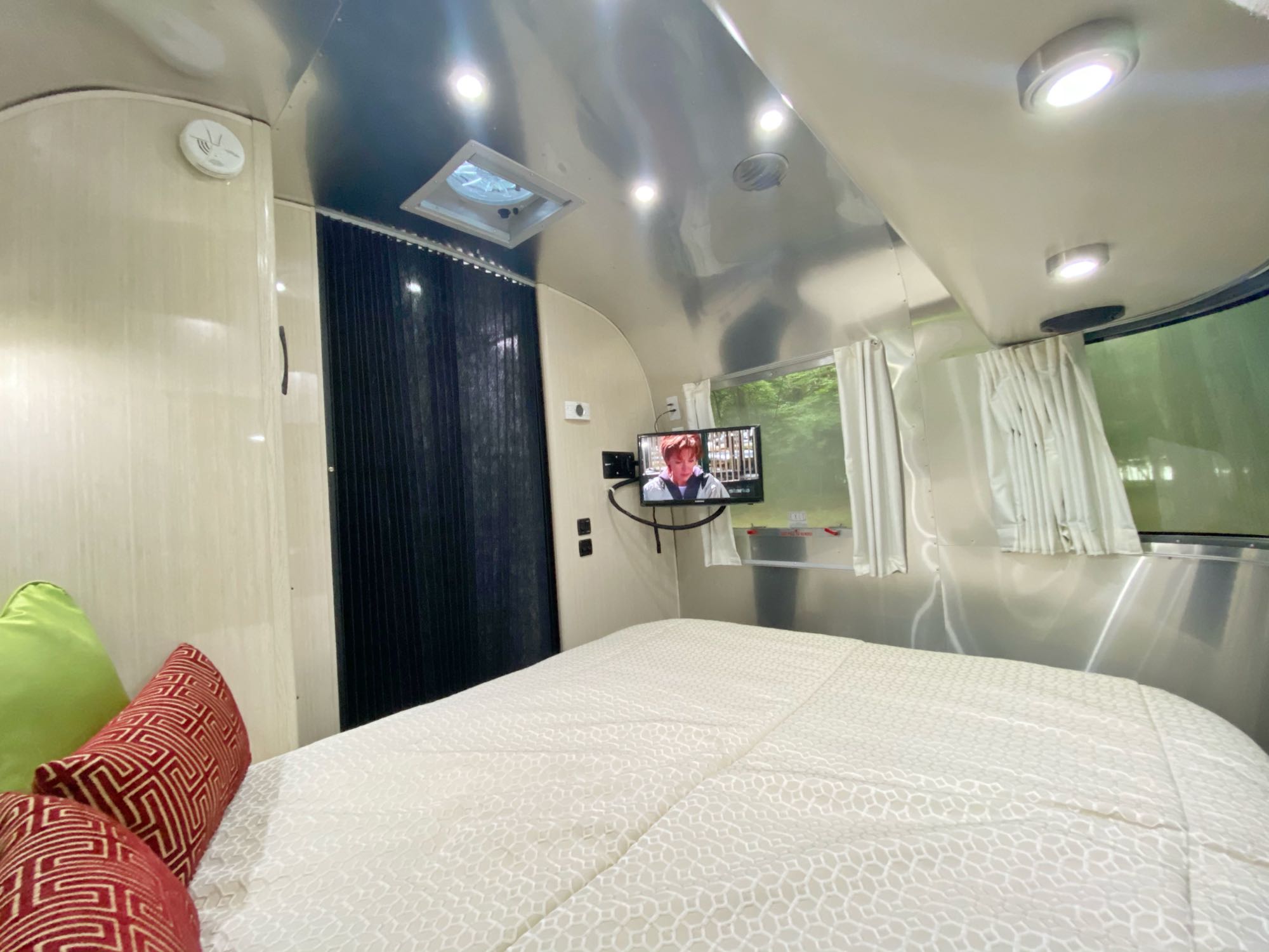 This RV rental offers a cozy bedroom with a white patterned bed, mounted TV, and bright interior lights.. Airstream International 2019