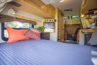 Cozy RV rental interior: A blue quilted bed with pillows, alongside windows & a compact living area.. Pleasure Way Excel 2006