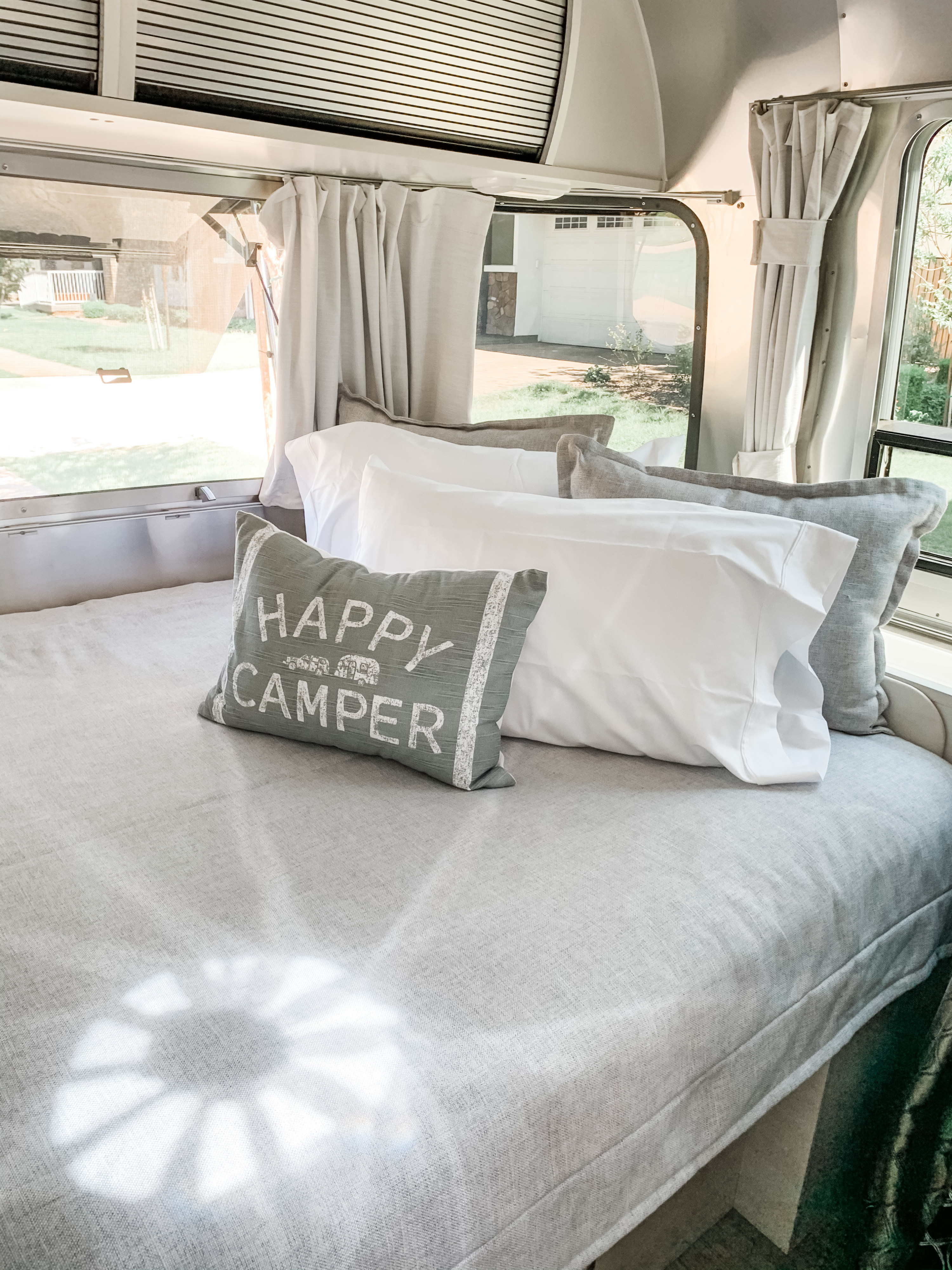 An inviting RV rental bedroom featuring a neatly made bed with white & grey pillows, set against a window with outdoor views.. Airstream Sport 2020