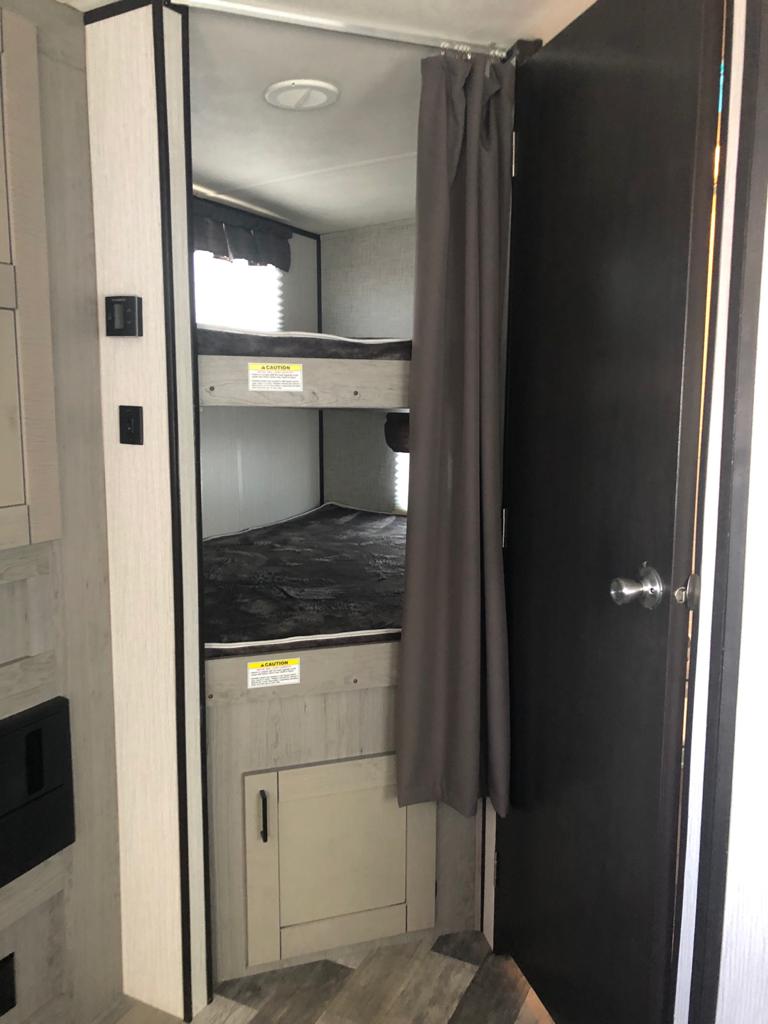 Inside an RV rental, a cozy bunk bed area with privacy curtain, a dark door, and cabinet below.. Heartland Other 2021