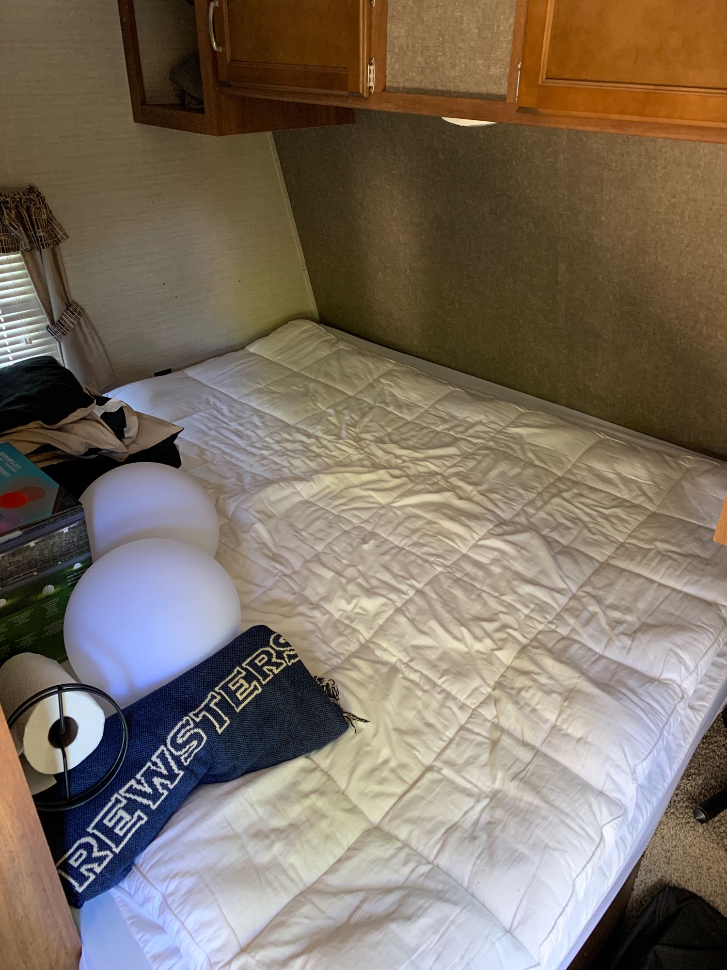 Cozy rv rental bedroom features a white bed, overhead cabinets, and window. Decorative lights & a "Rewsters" blanket are on the bed.. Keystone Springdale 2017
