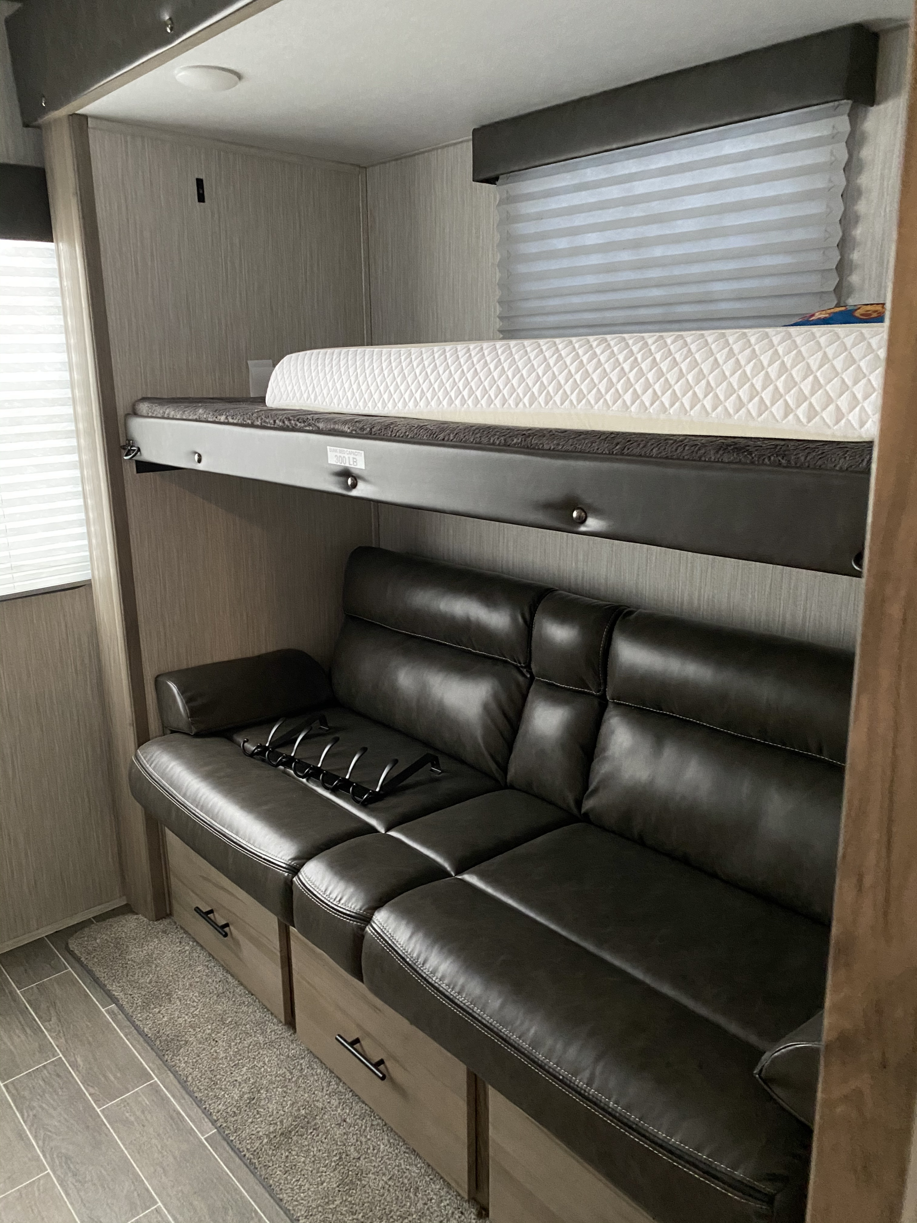 Inside an RV rental: a top bunk bed with a quilted mattress sits above a dark leather-like sofa with under-seat storage.. Forest River Other 2020