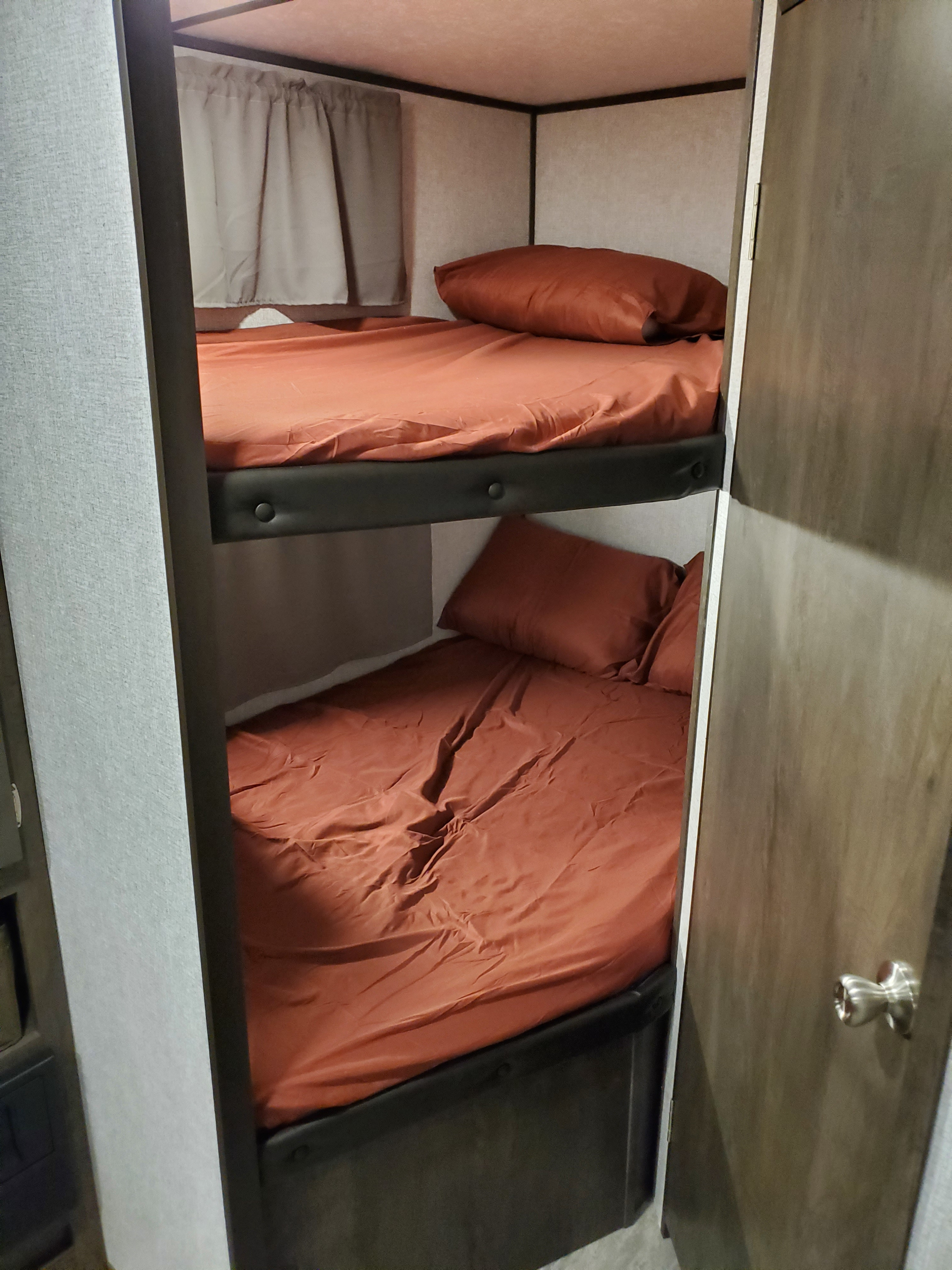 Inside an RV rental: two bunk beds with rust-colored sheets and pillows, offering a compact sleeping space for travelers.. Dutchmen Aspen Trail 2020