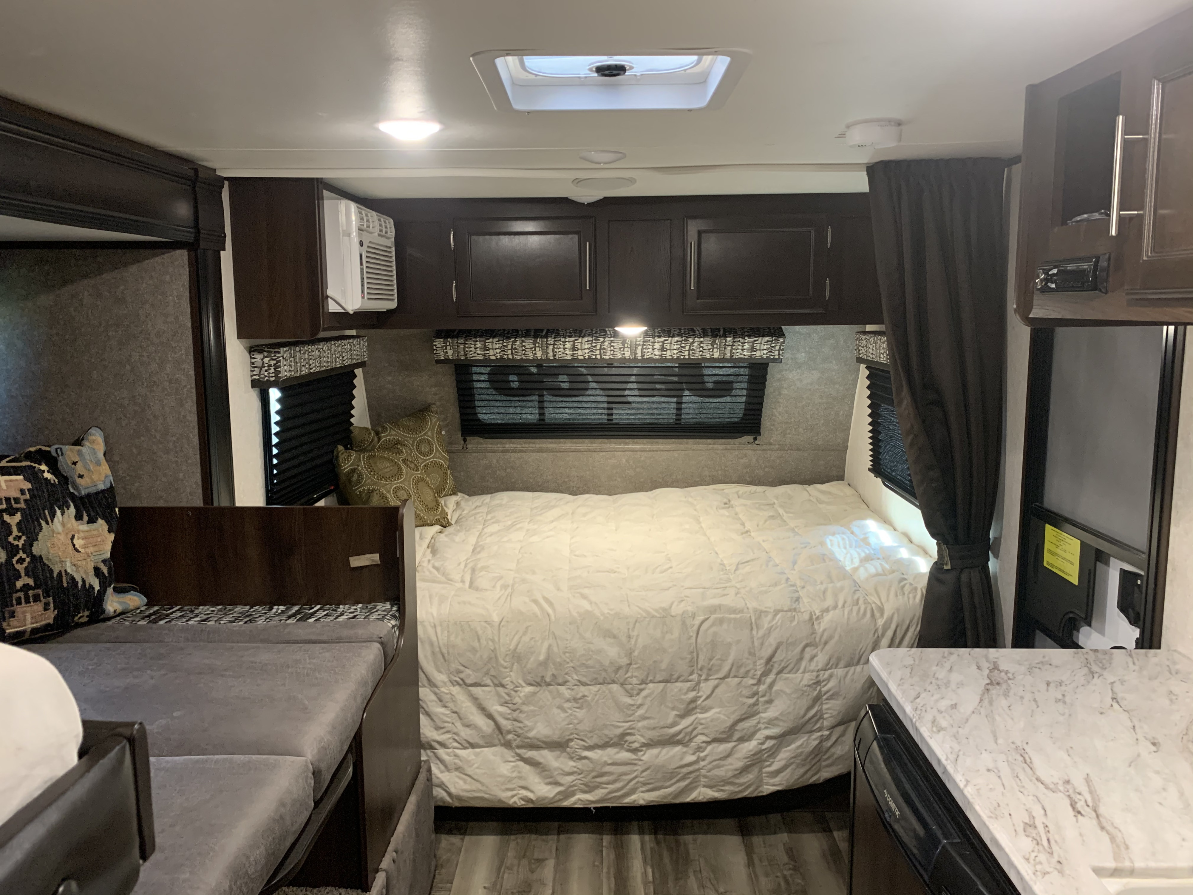 RV rental's cozy interior: bedroom with large bed, AC unit, overhead cabinets, and compact living area.. Jayco Other 2019