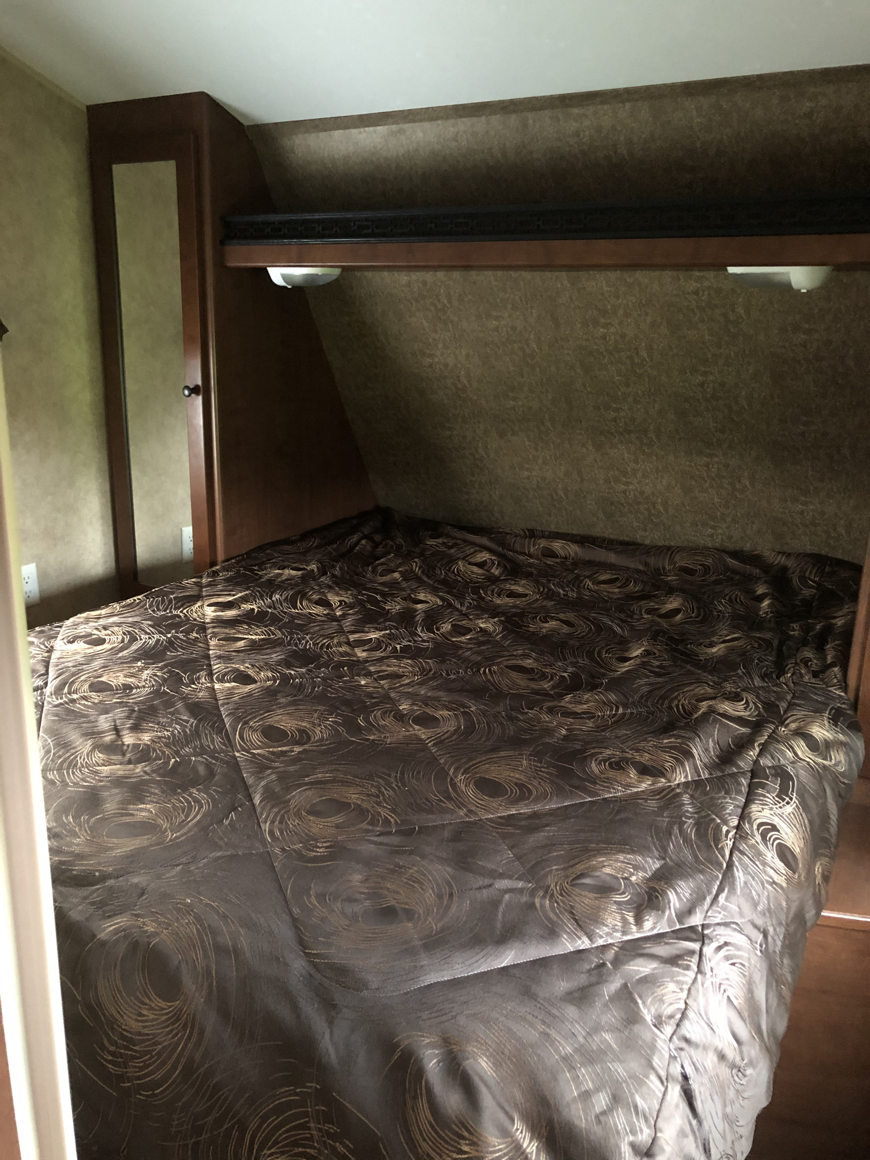 Comfortable RV rental bedroom featuring a patterned bedspread, overhead lighting, and compact storage.. Dutchmen Other 2013