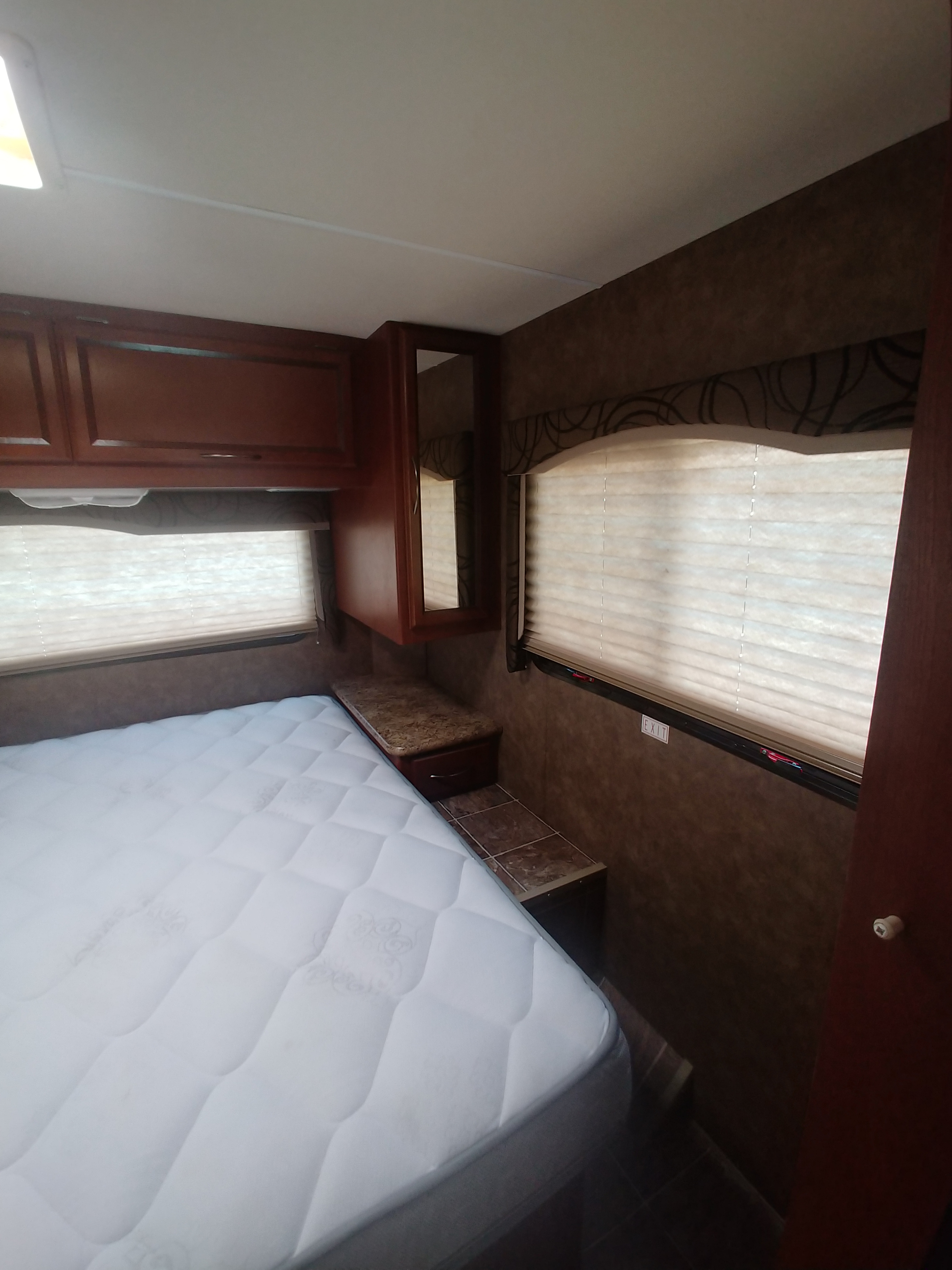 Cozy RV rental bedroom with a white mattress, overhead wood cabinets, and window blinds.. Thor Motor Coach Freedom Elite 2013