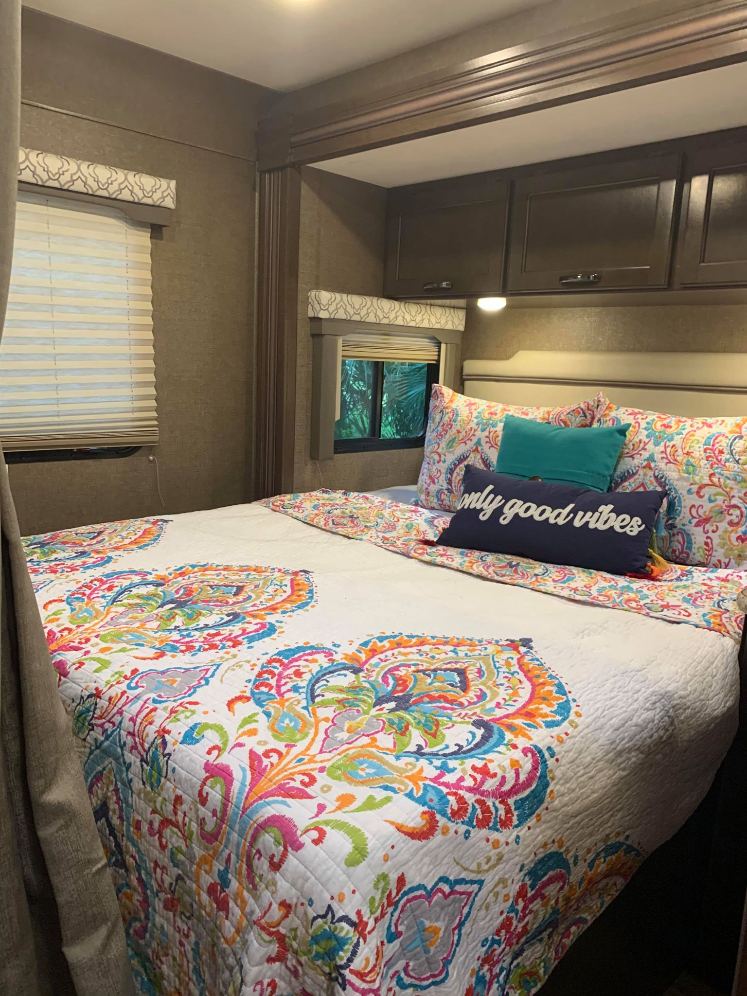 Explore this vibrant RV rental bedroom! Features a cozy bed with colorful quilt, "only good vibes" pillow, and ample storage.. Thor Motor Coach Freedom Elite 2019