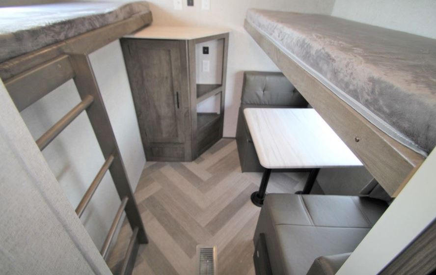 Inside an RV rental: view of bunk beds with ladder, compact dinette with table, and corner storage unit.. Forest River Wildwood 2021