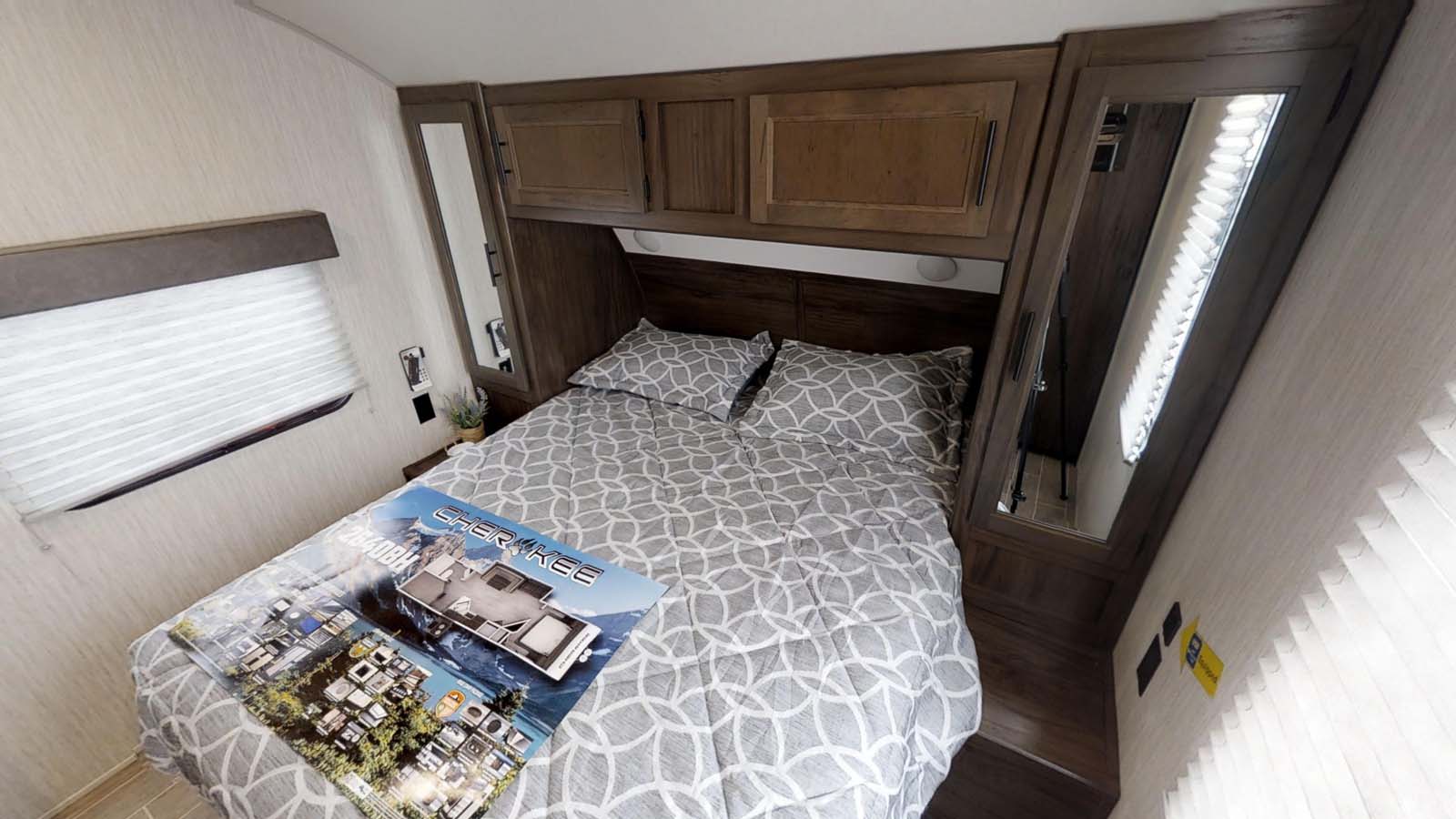 Inside a modern RV rental, this bedroom features a bed with geometric bedding, wooden cabinets, and mirrored wardrobes.. Forest River Cherokee 2019