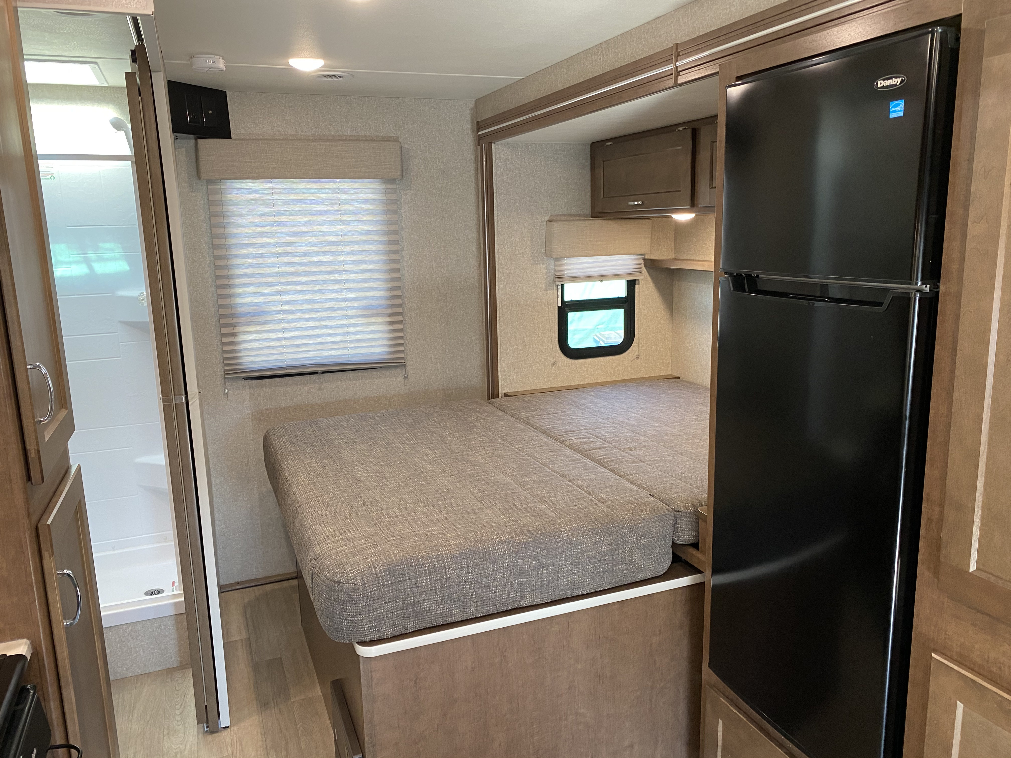 Inside an RV rental: view of the bed, built-in refrigerator, and separate shower stall. Compact & functional.. Winnebago Vita 2020