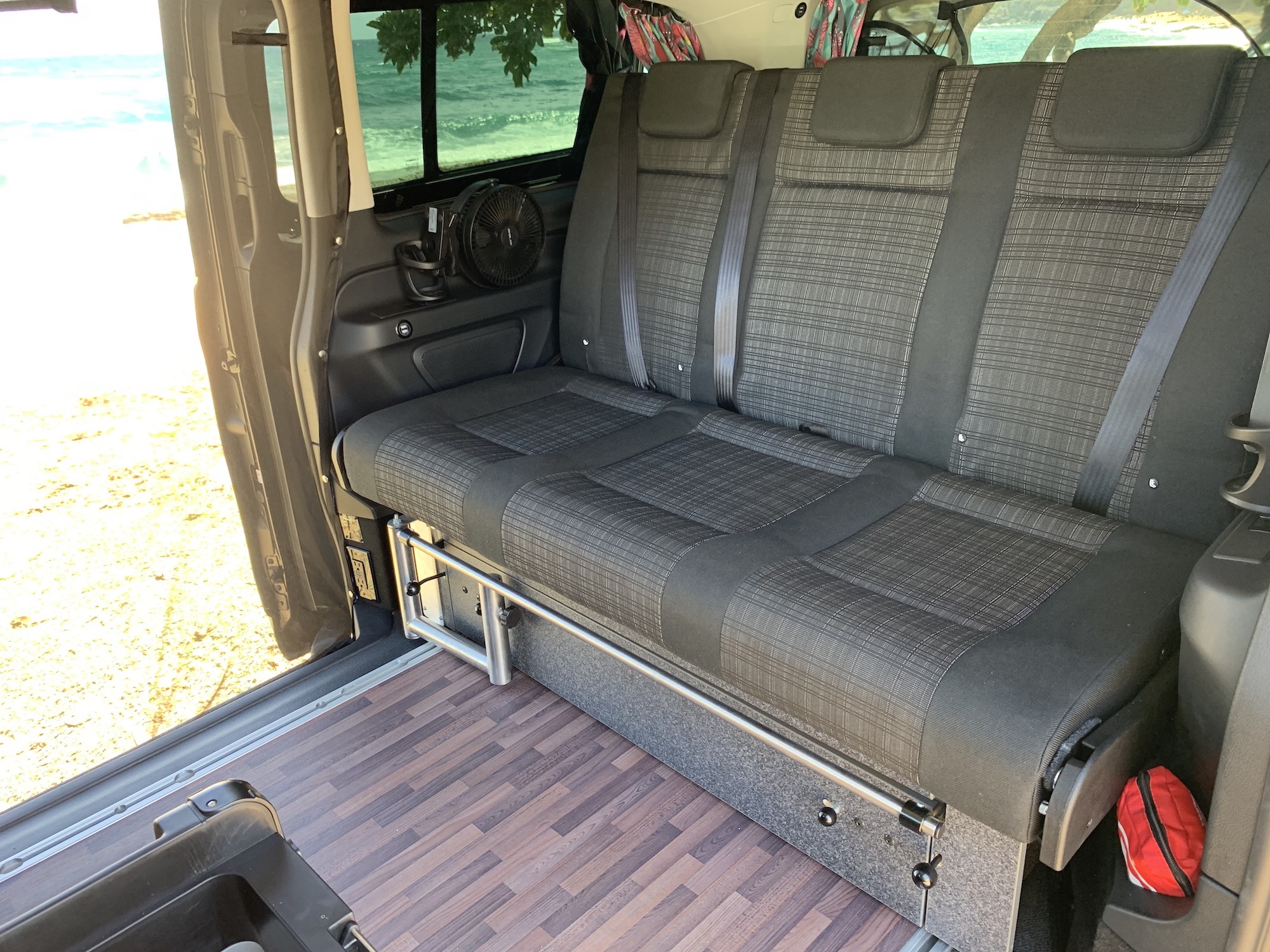 Spacious RV rental interior with a versatile bench seat (converts to bed) and stunning ocean view through the open door.. Mercedes Metris Pop-Top 2019