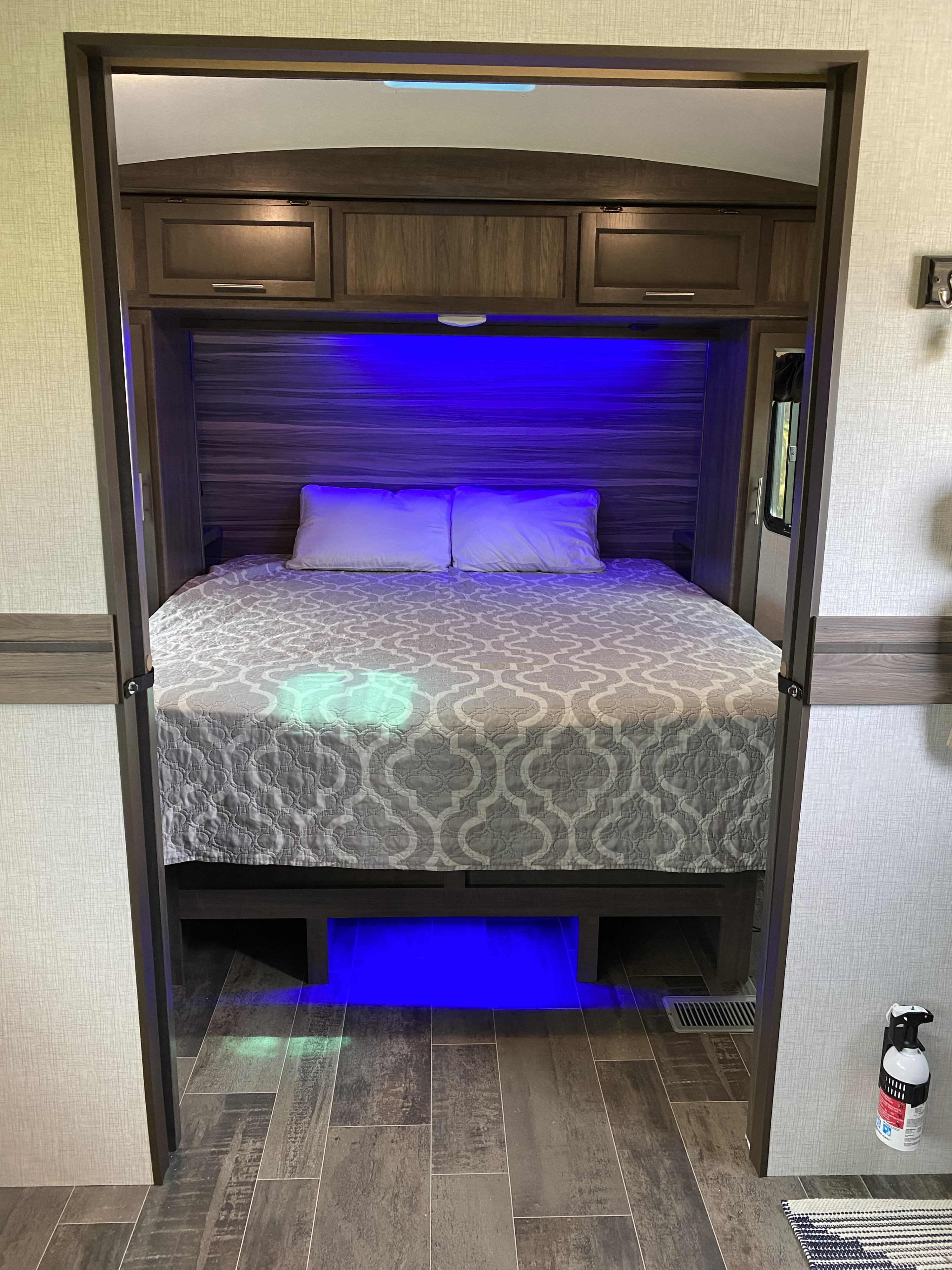 Cozy RV rental bedroom with blue ambient lighting, bed, storage, and a fire extinguisher, viewed from the doorway.. Crossroads Sunset Trail Super Lite 2020