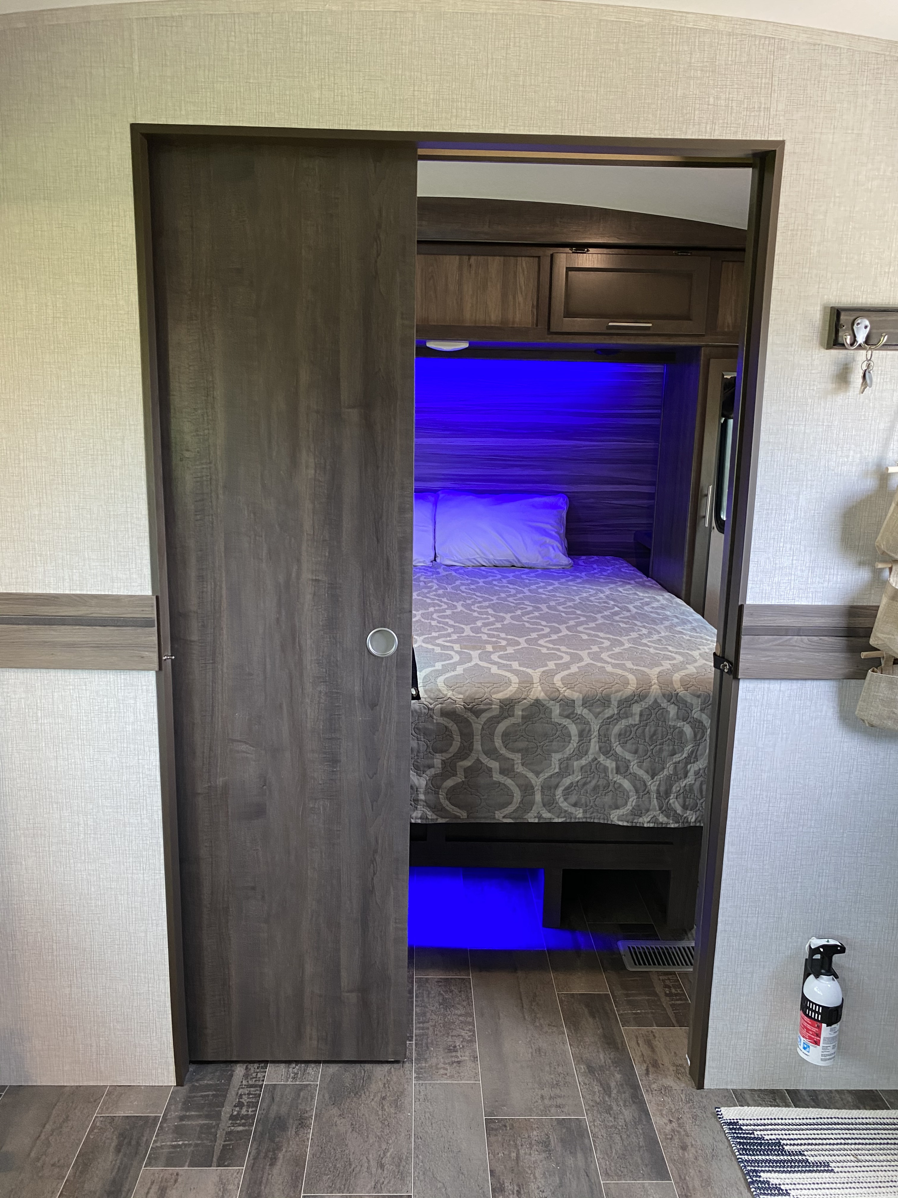 Inside an RV rental: a modern bedroom with a partially open sliding door, bed, and inviting blue LED lighting.. Crossroads Sunset Trail Super Lite 2020