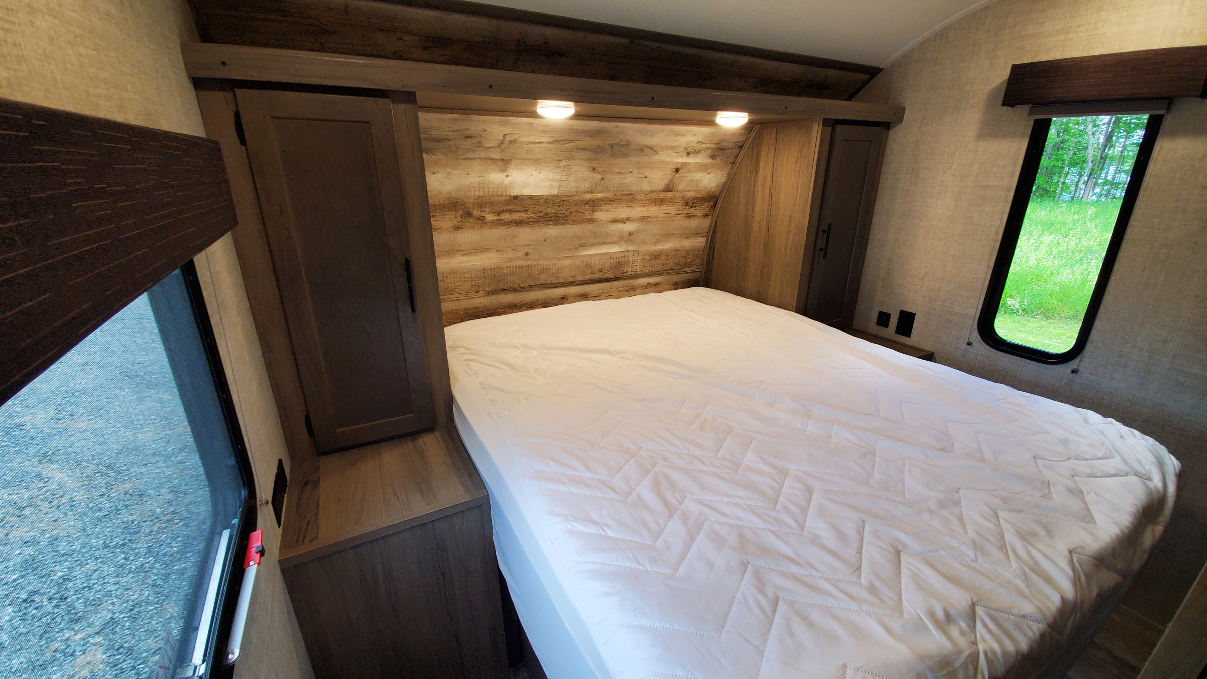 Cozy RV rental bedroom featuring a comfortable bed, warm wood interior, and scenic windows, ready for your next adventure.. Gulf Stream Trailmaster 2021