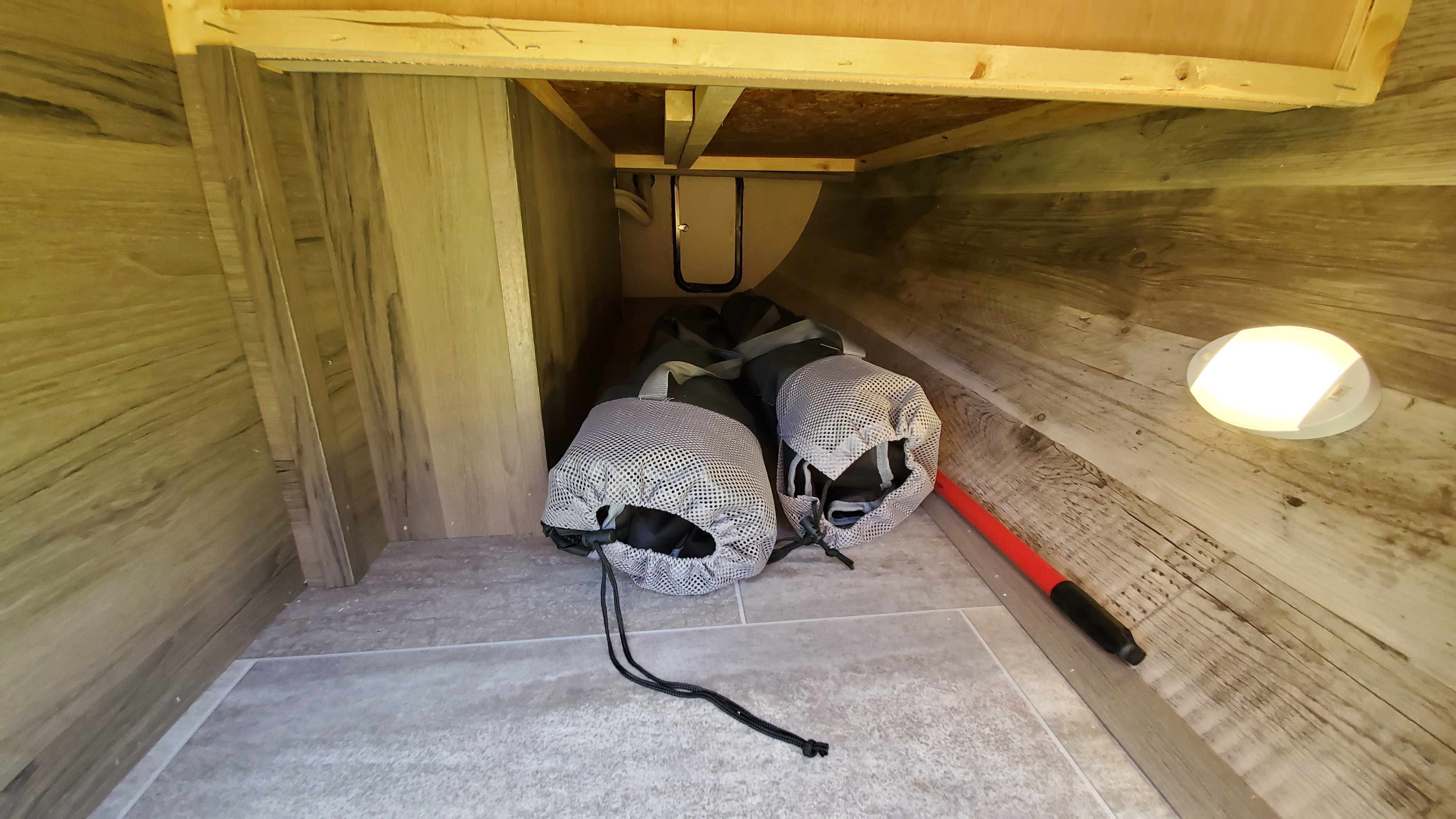 RV rental: practical under-storage with wood-look walls, light gray tiled floor, a light, and gear in mesh bags.. Gulf Stream Trailmaster 2021