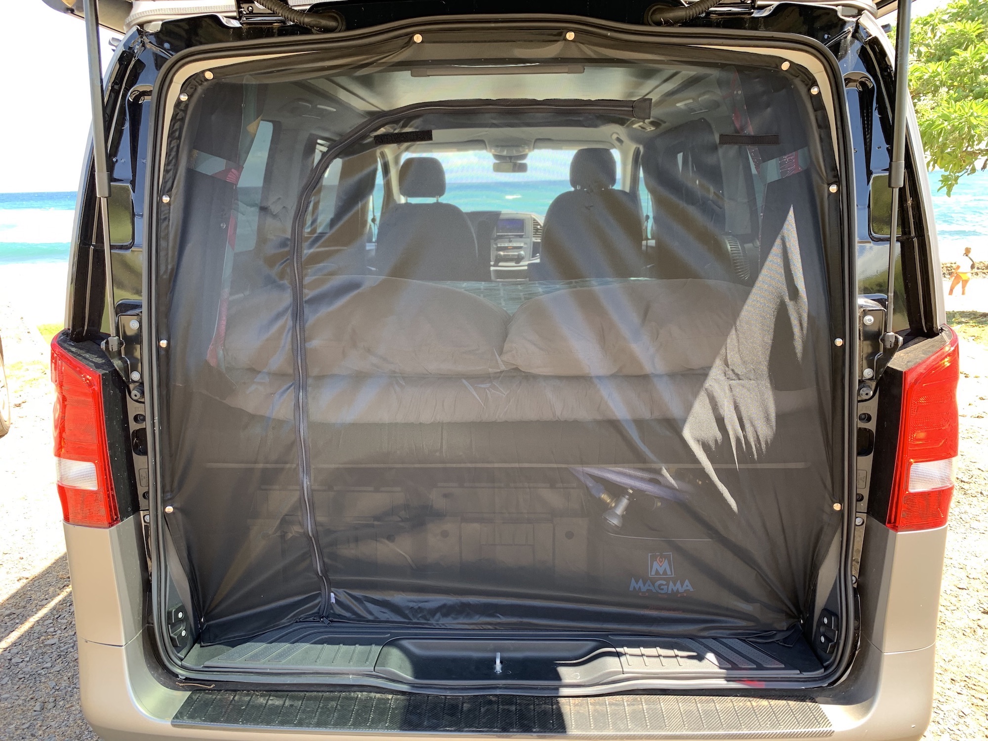 RV rental van's rear hatch features a bug screen, revealing a cozy bed and an ocean view through the front.. Mercedes Metris Pop-Top 2019
