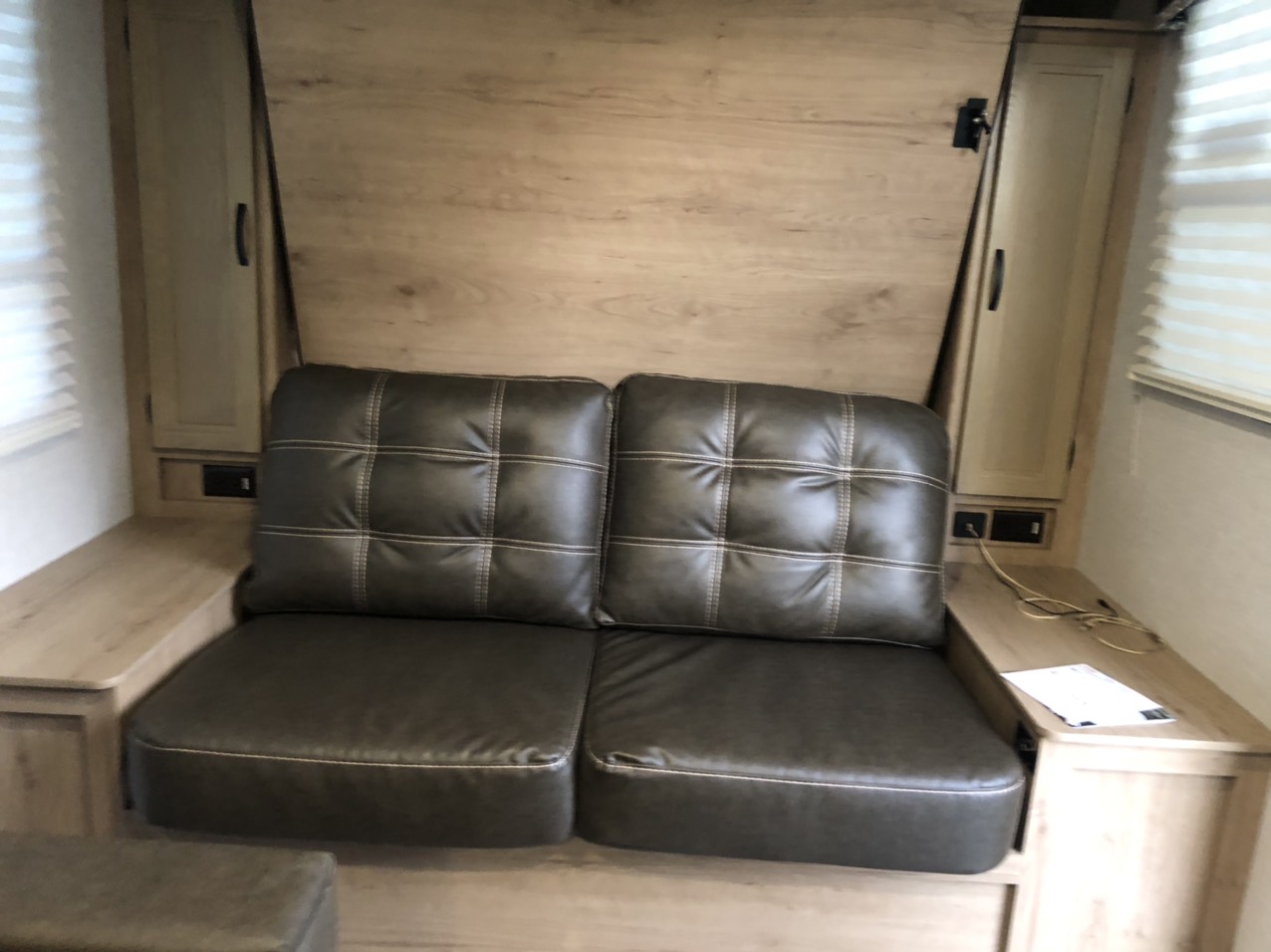 Light wood interior of an RV rental shows a dark brown sofa, convertible to a bed, flanked by storage cabinets.. Winnebago Minnie Winnie 2021