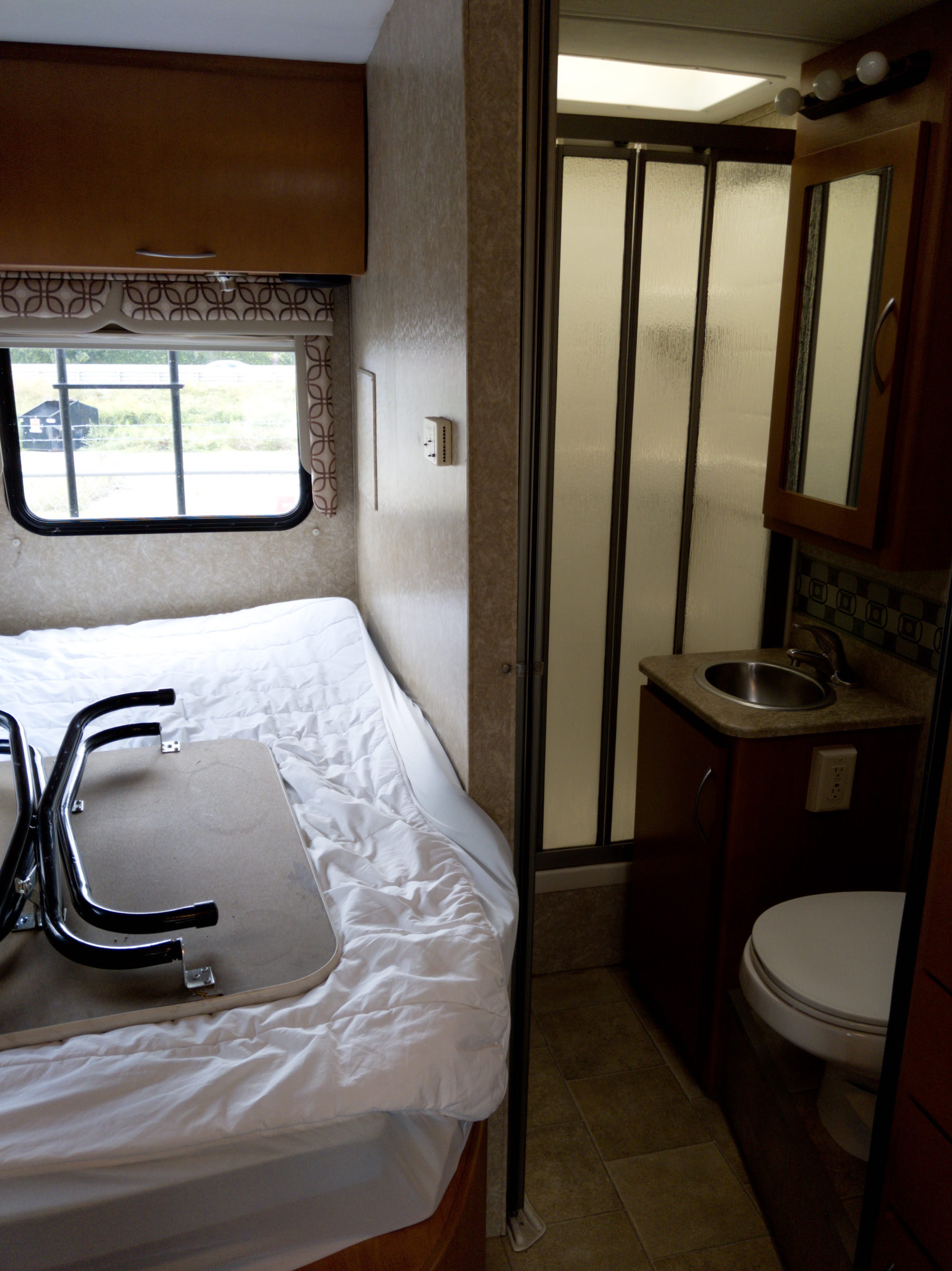 Compact rv rental interior featuring a bed, window, and small bathroom with shower, sink, and toilet.. Thor Motor Coach Four Winds Siesta Sprinter 2011