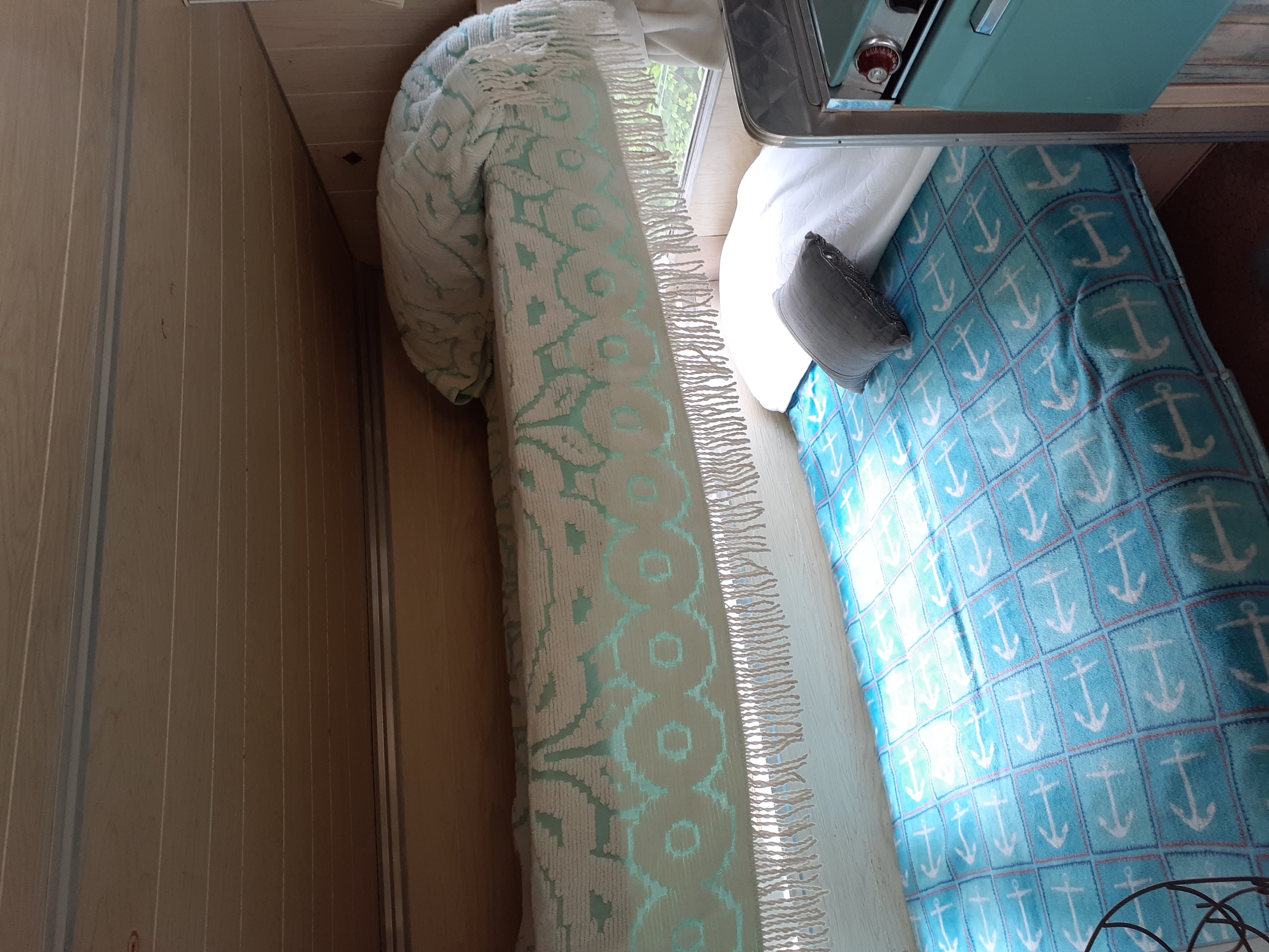 Cozy RV rental interior with a blue anchor blanket, patterned throw, and compact kitchen area.. Aristocrat Lo-Liner 1965