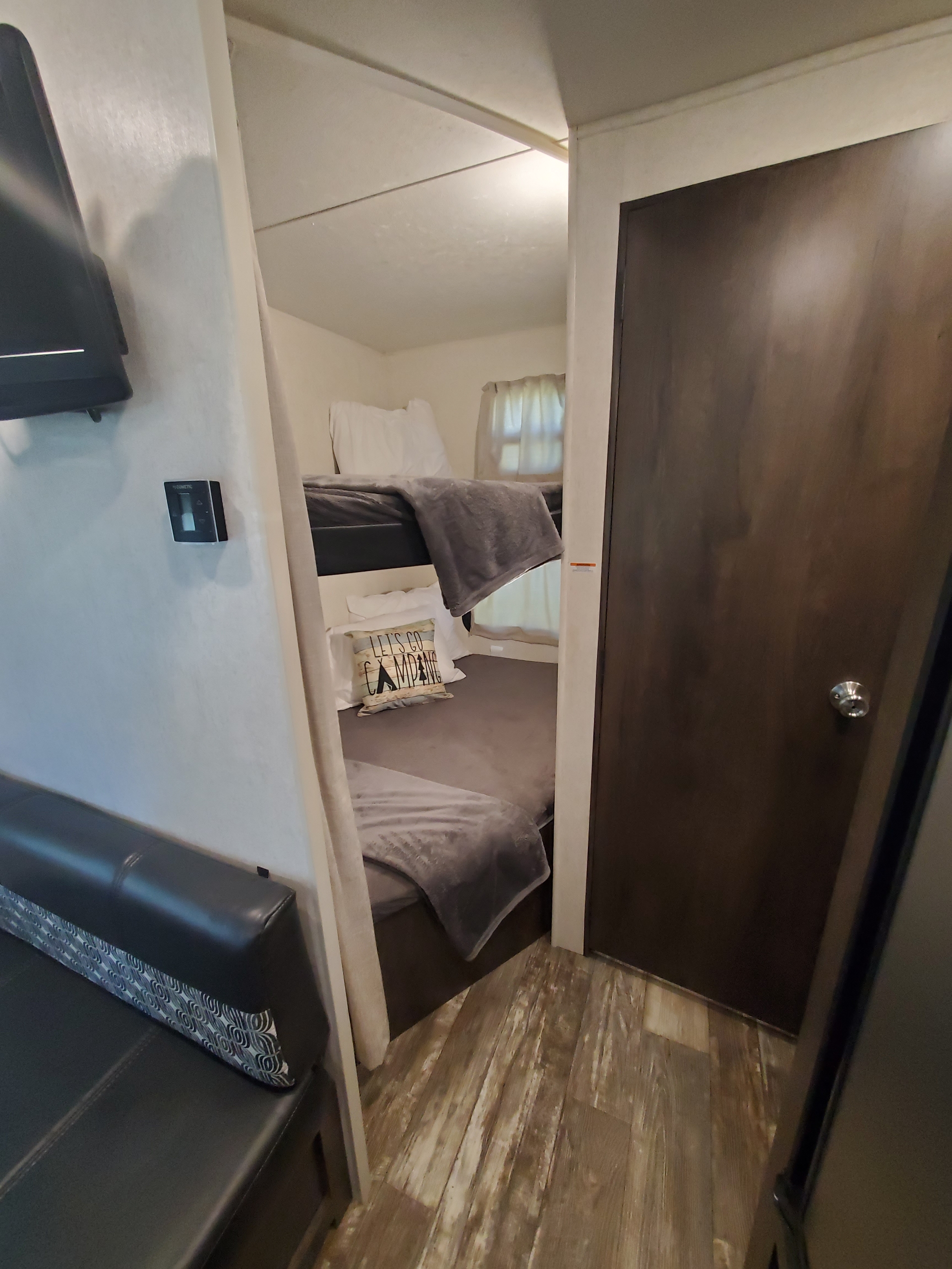 Inside an RV rental: a bunk bed area with grey blankets, a "Let's Go Camping" pillow, a black sofa, and a wall-mounted Dometic thermostat.. Starcraft Autumn Ridge 2019