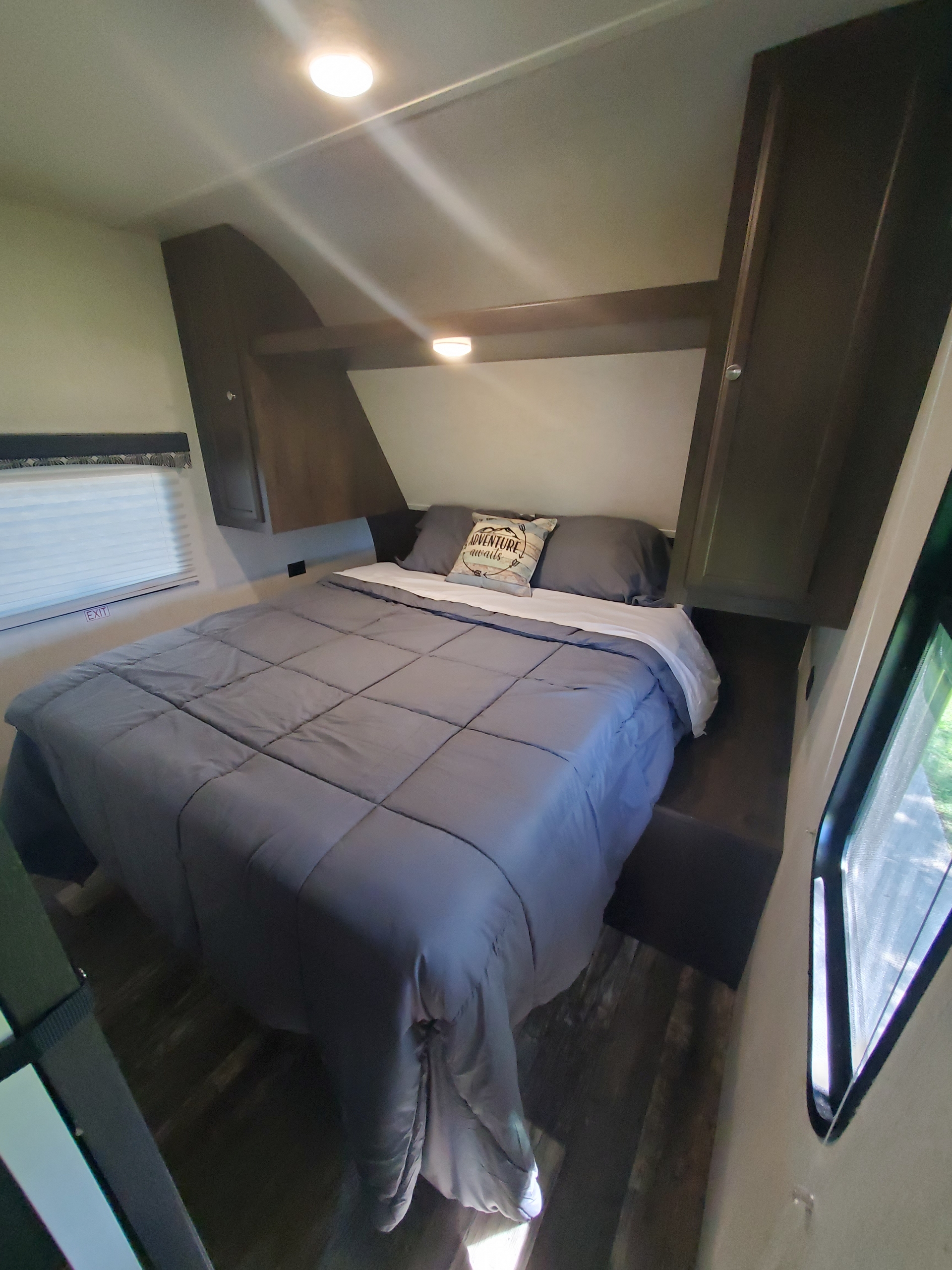 This RV rental offers a cozy bedroom featuring a neatly made bed with dark gray bedding, an "ADVENTURE awaits" pillow, and ample overhead storage.. Starcraft Autumn Ridge 2019