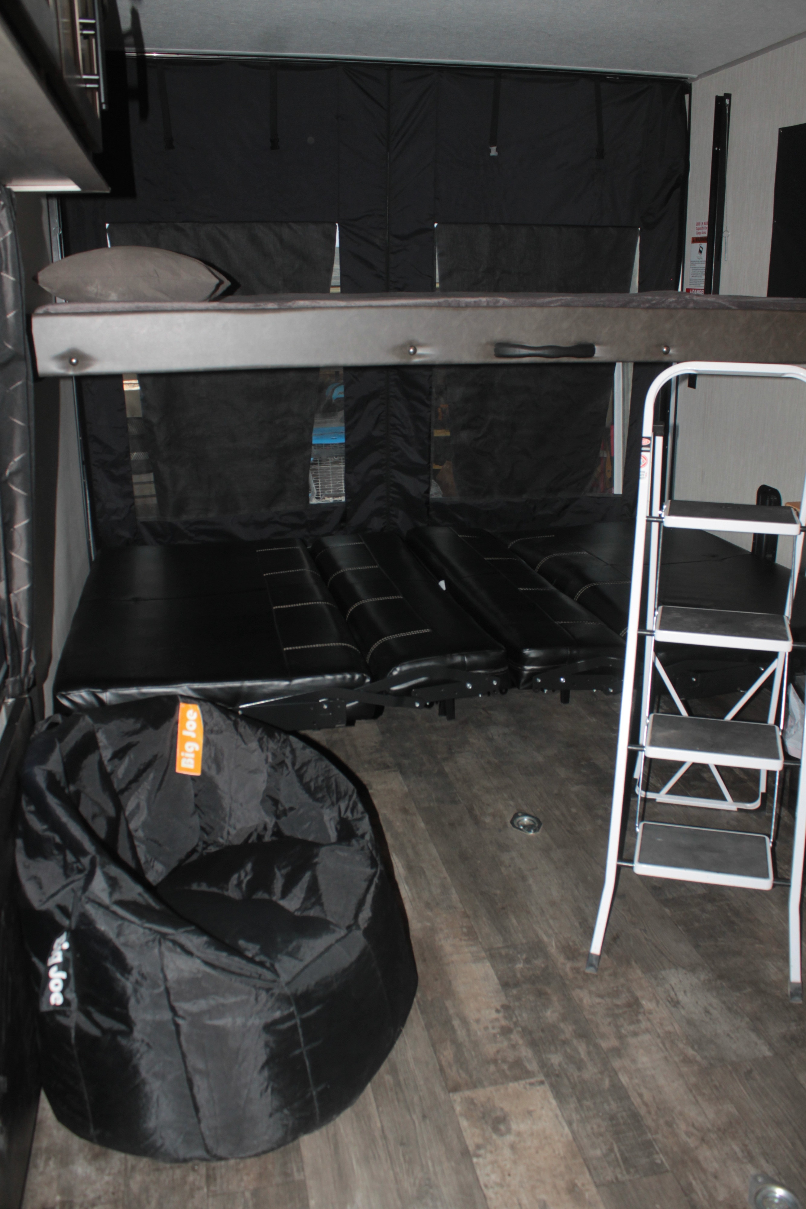 RV rental with black bunk beds, a convertible sofa below, a ladder, and bean bag chair on wood-look floor.. Forest River Cherokee Wolf Pack 2021