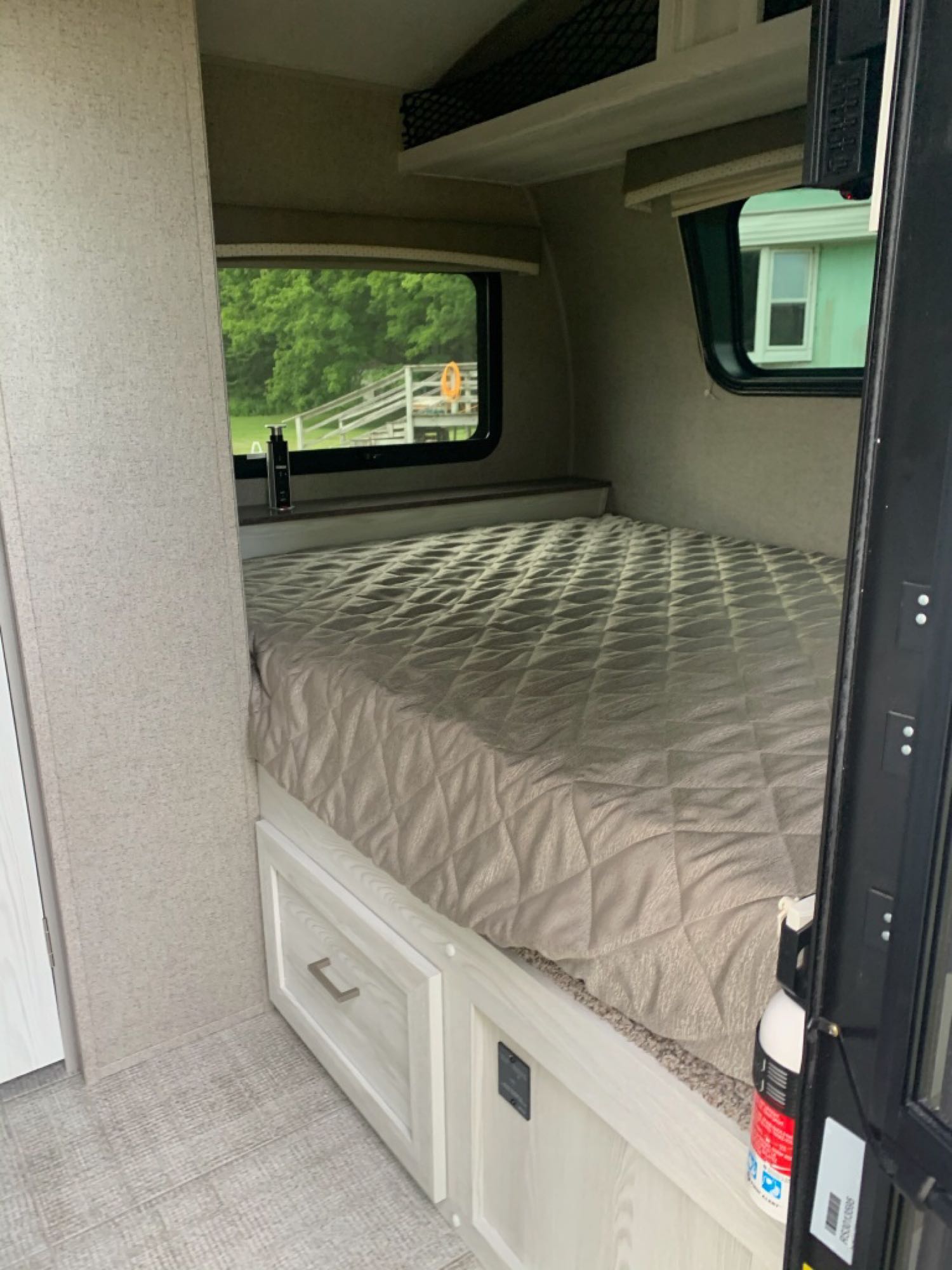 Interior of an RV rental bedroom showing a large bed with quilted cover, under-bed drawers, and windows with outdoor views.. Forest River Other 2021