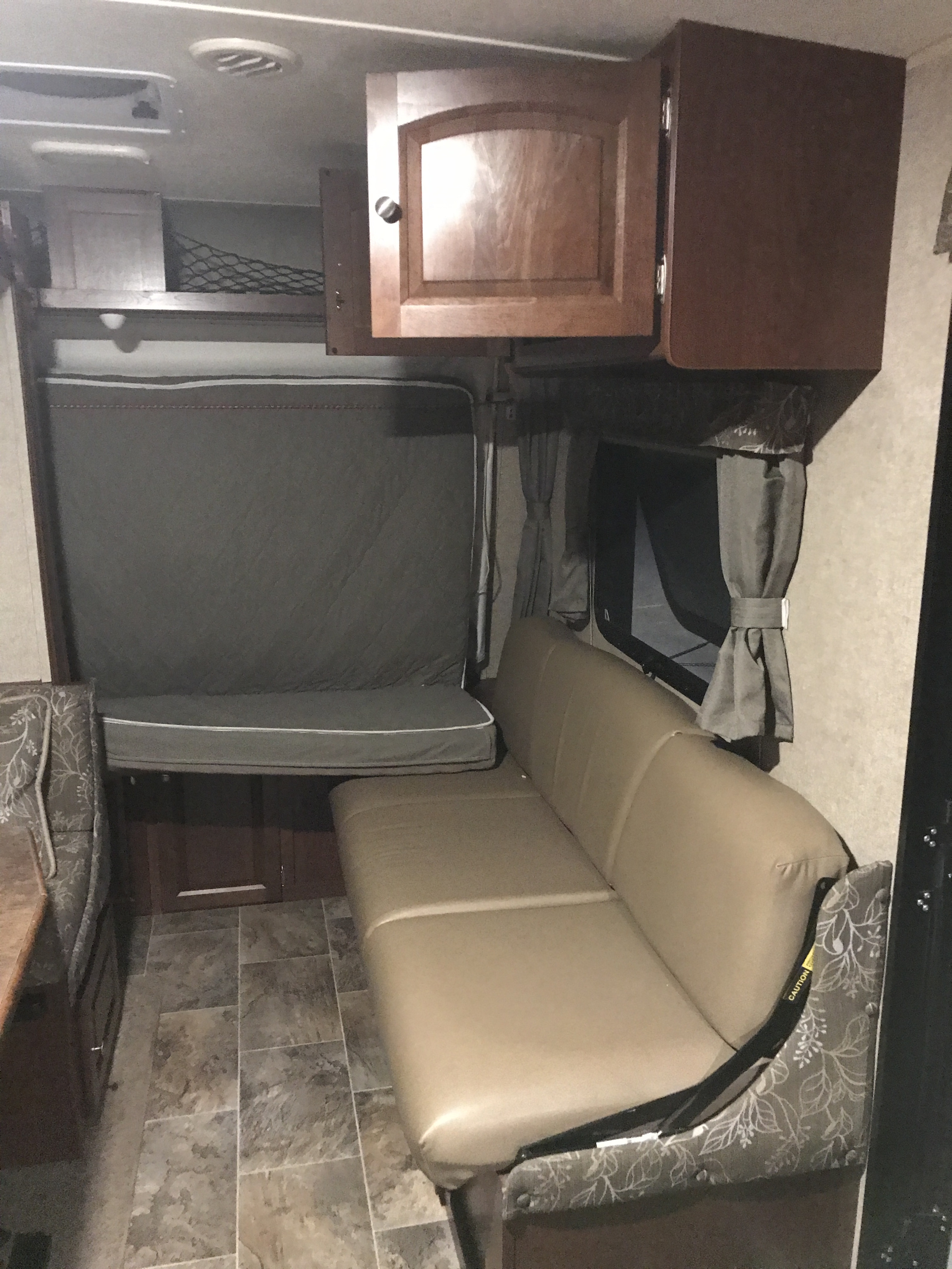 This RV rental interior features a beige dinette, a gray convertible bed, wood cabinets, and tile-look flooring.. Forest River Rockwood Roo 2016
