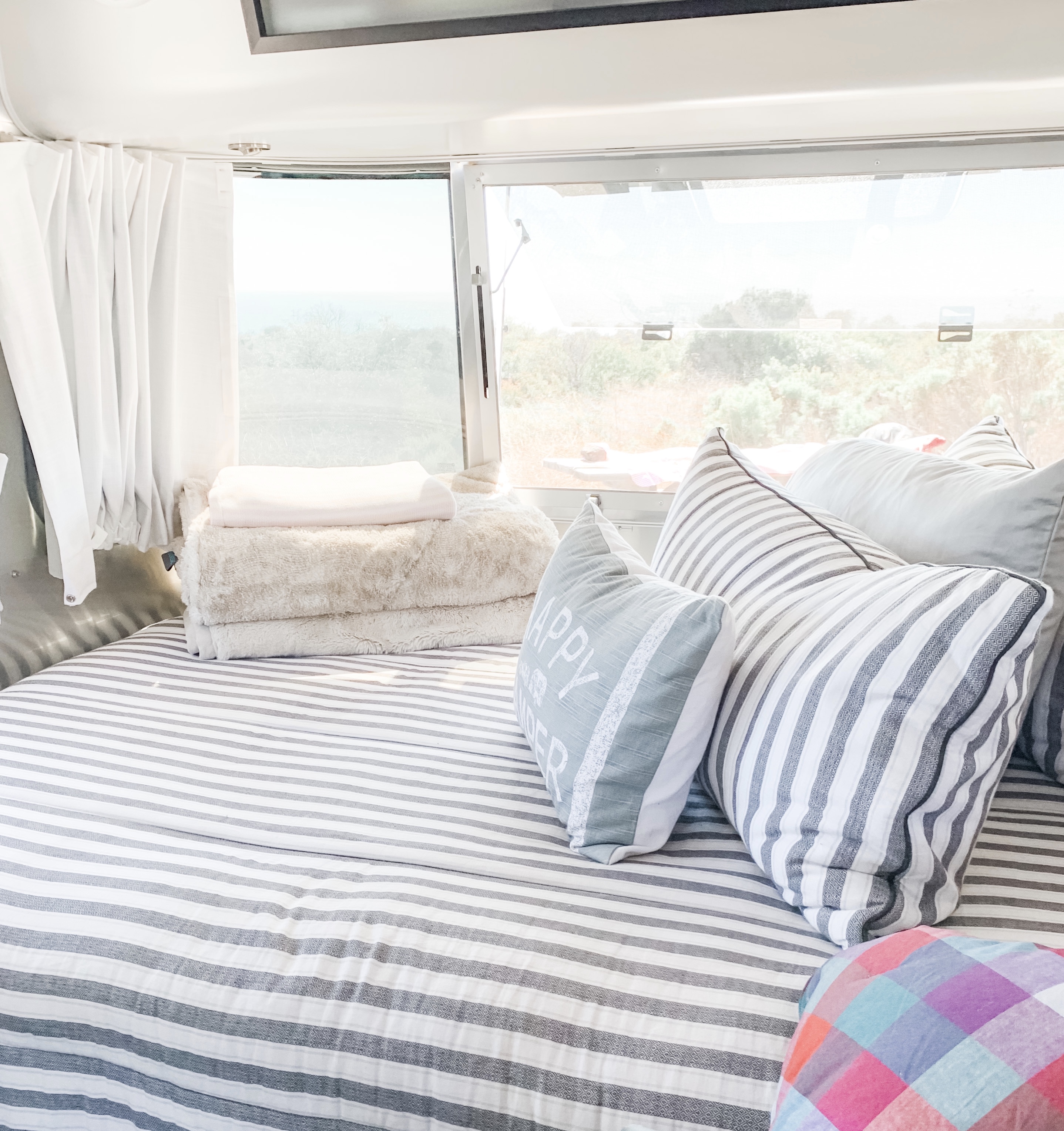 Cozy RV rental bedroom with striped bedding, pillows, and a scenic window view of nature.. Airstream Caravelle 2021