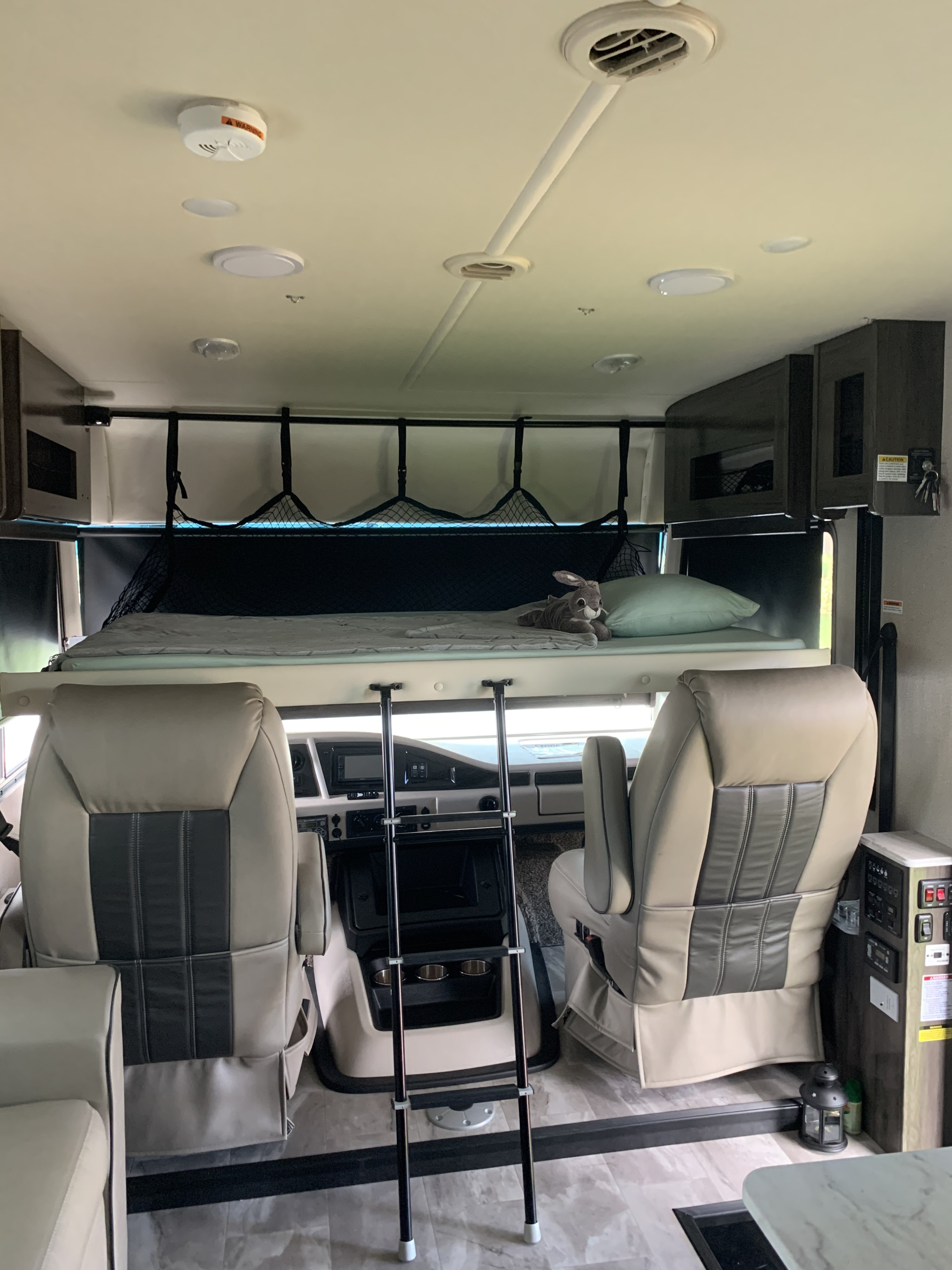 Interior of an RV rental: front cabin with swiveling captain's chairs and an overhead bunk bed with a ladder.. Holiday Rambler Admiral 2021