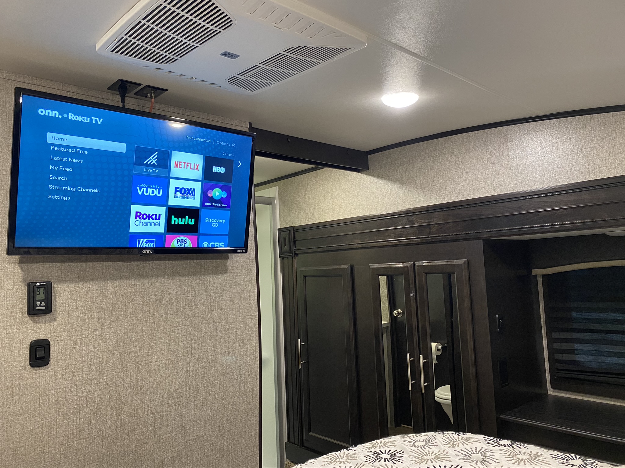 Inside an RV rental: A bedroom with an onn. Roku TV, AC unit, and dark wood cabinetry. The thermostat reads 91 degrees.. Jayco Eagle 2020