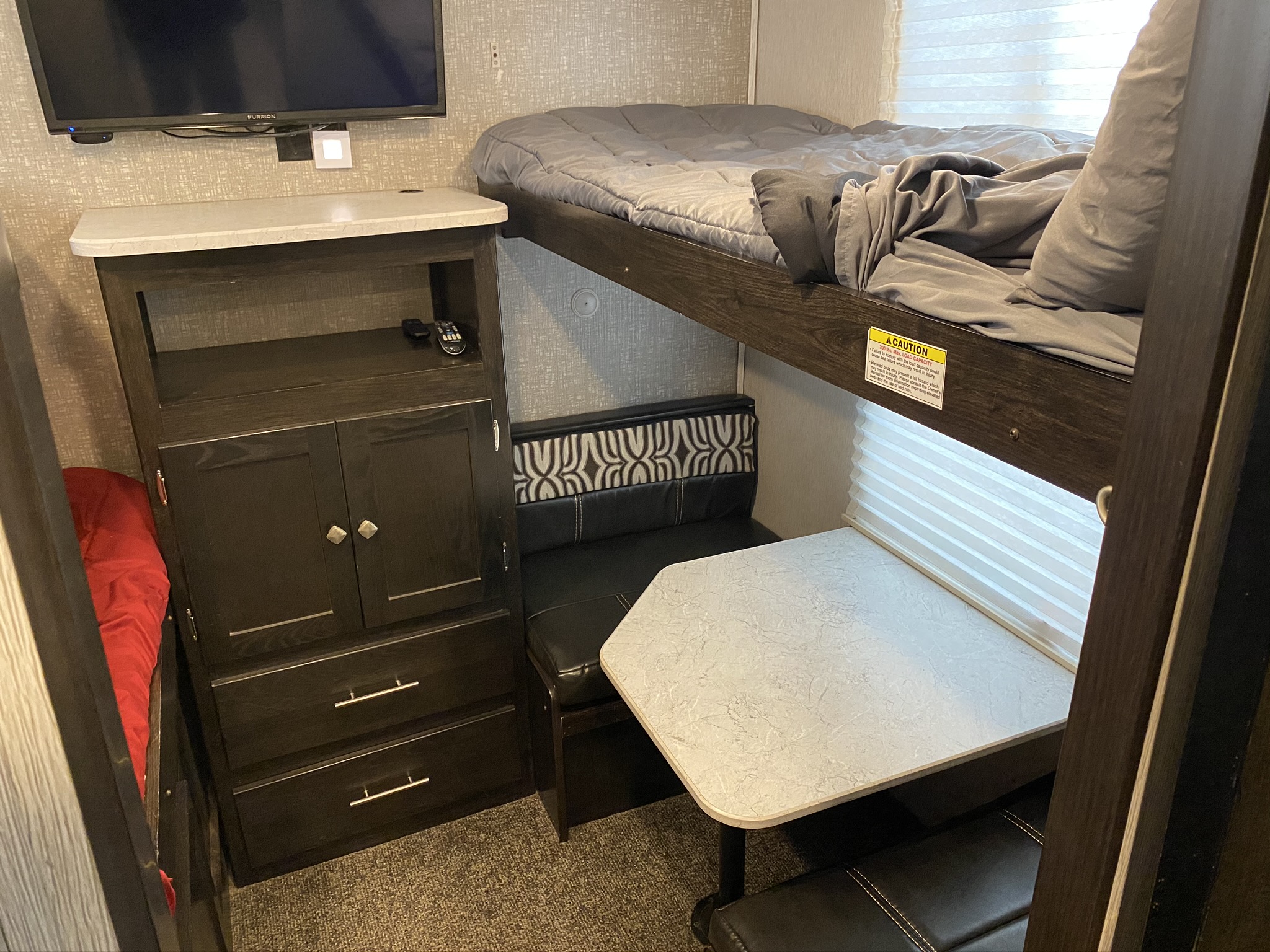 Compact RV rental interior features bunk beds, a dinette, and storage with a TV, maximizing space for travel.. Heartland North Trail 2020